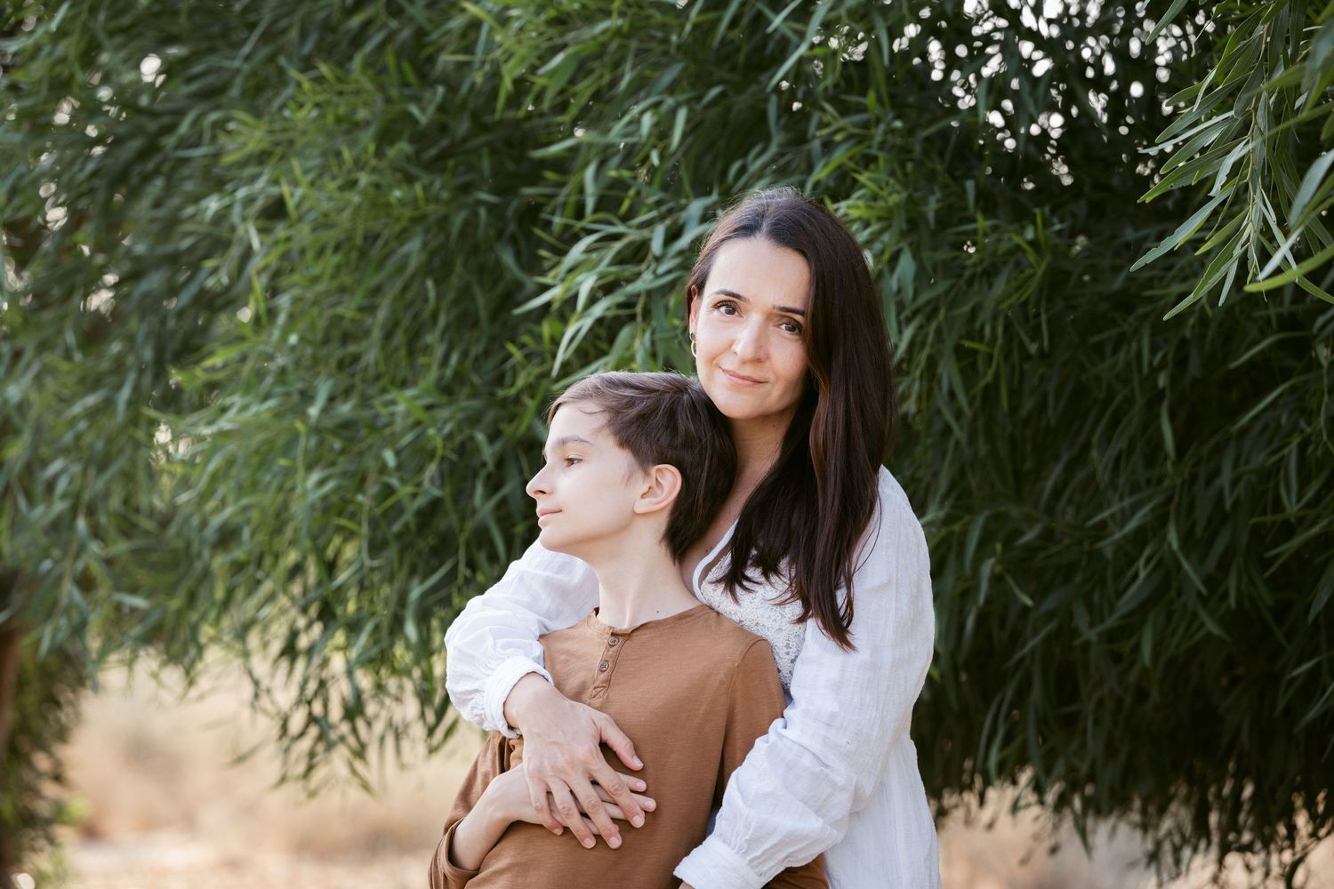 A tender moment captured under willow trees with soft natural lighting.