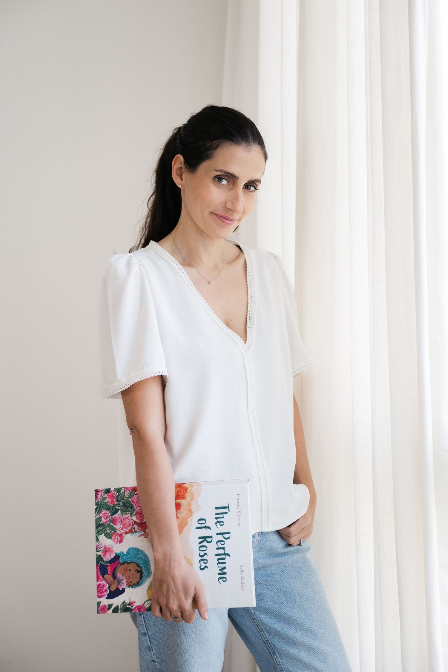 Woman in white blouse holding books against bright interior wall.