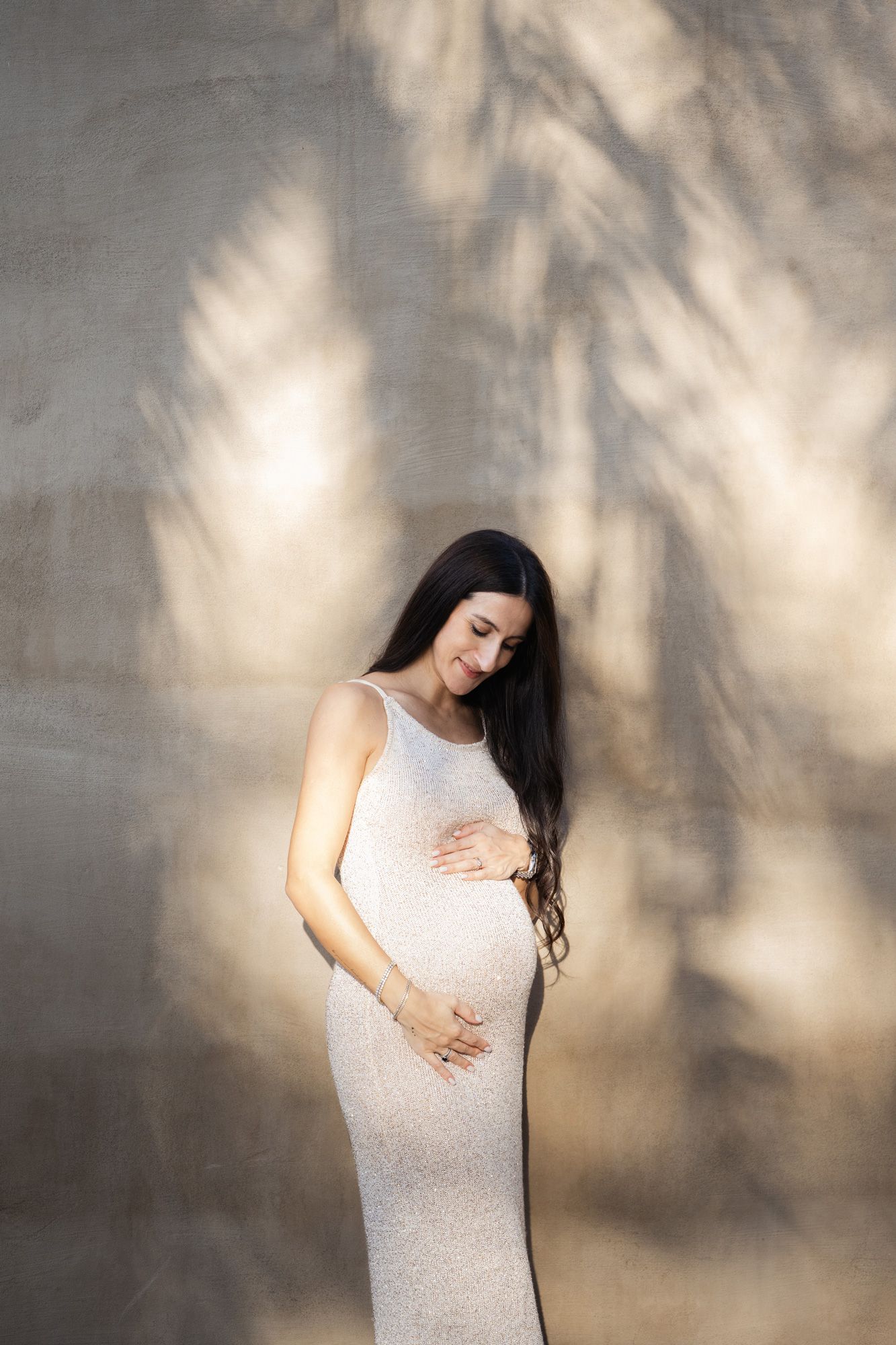 Artistic maternity photo series showing silhouetted figure in white dress against textured wall with dappled lighting.