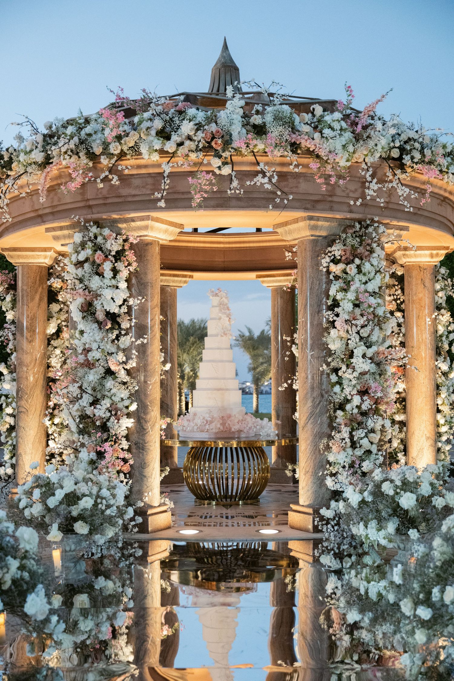 Elegant wedding gazebo decorated with white floral arrangements and crystal chandeliers overlooking the water.