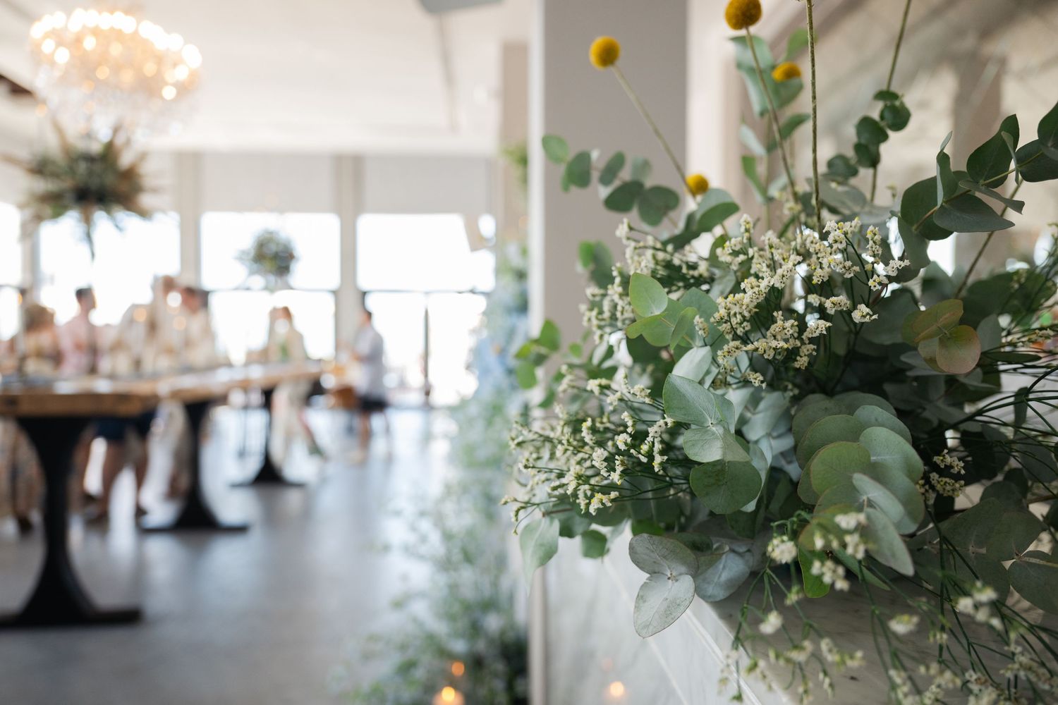 Elegant floral arrangements with eucalyptus and white flowers decorate a bright event space.