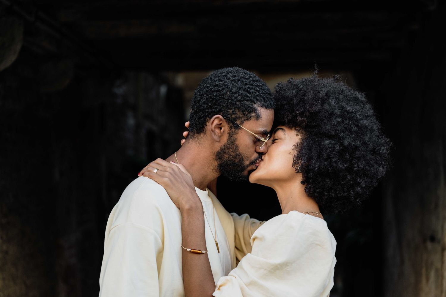 Affectionate couple in white outfits sharing intimate moments in dark setting.