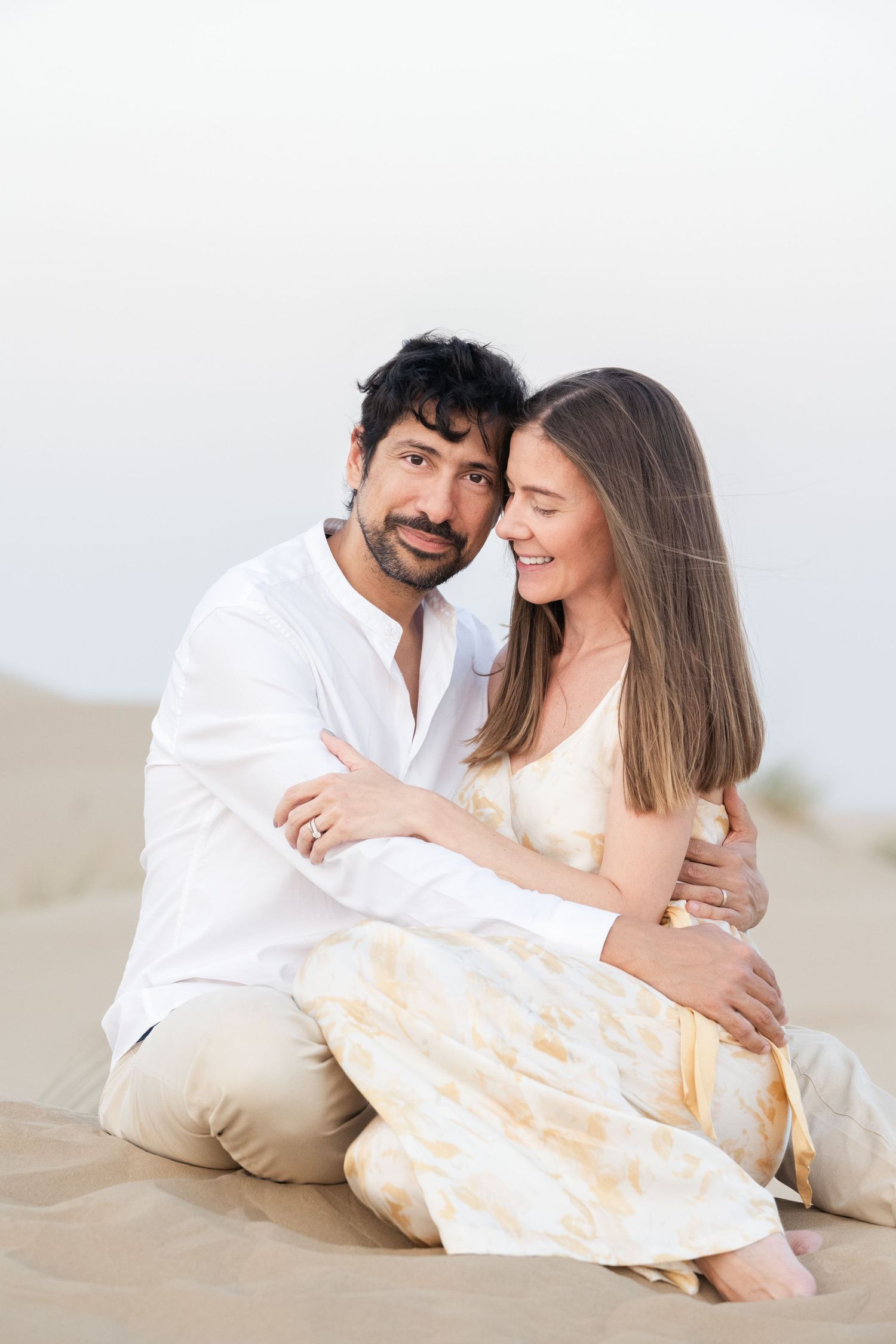Couple laying together on sandy beach during romantic desert photoshoot.