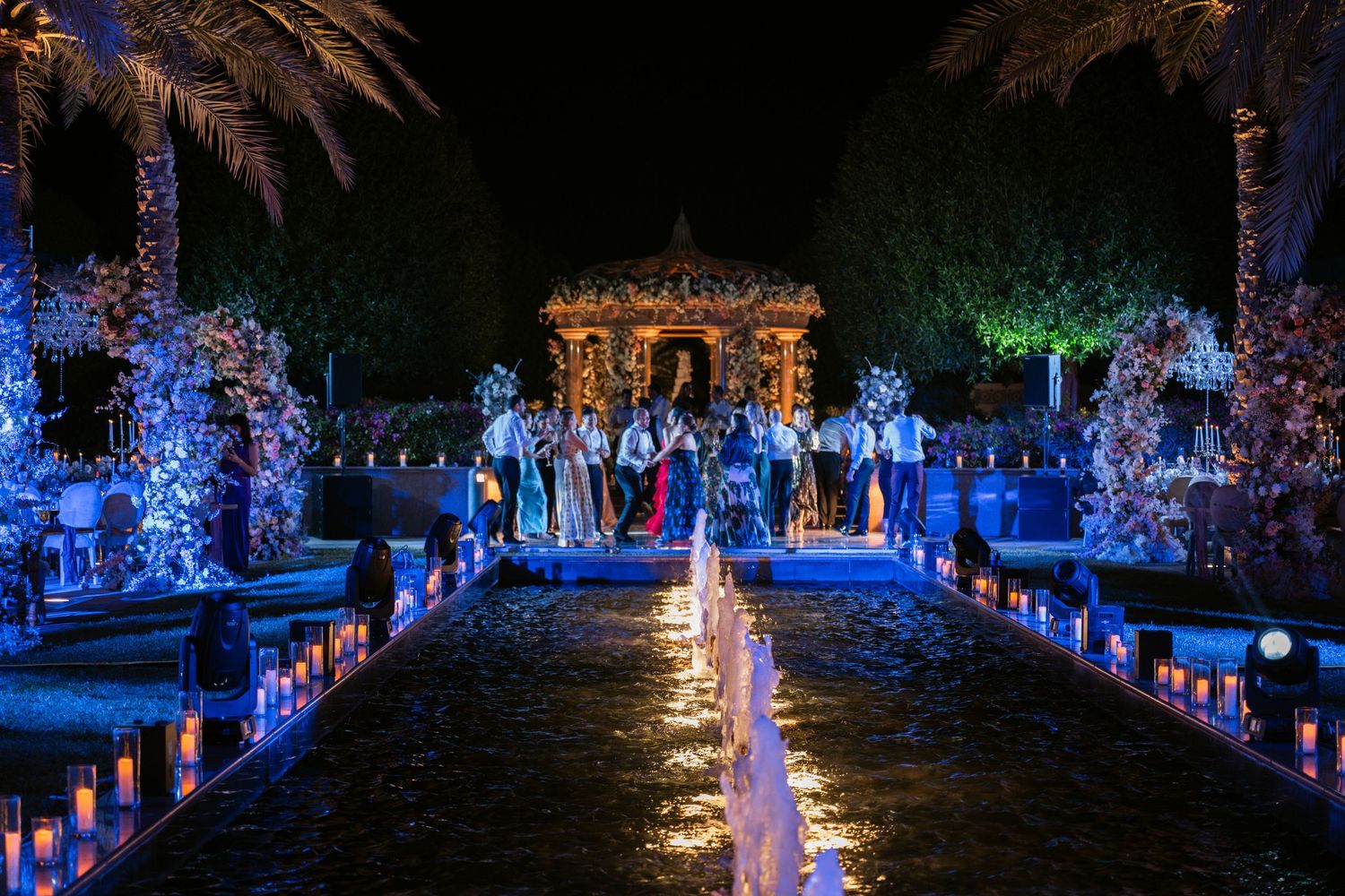 Outdoor wedding venue illuminated with blue LED lights and palm trees creating a magical atmosphere.