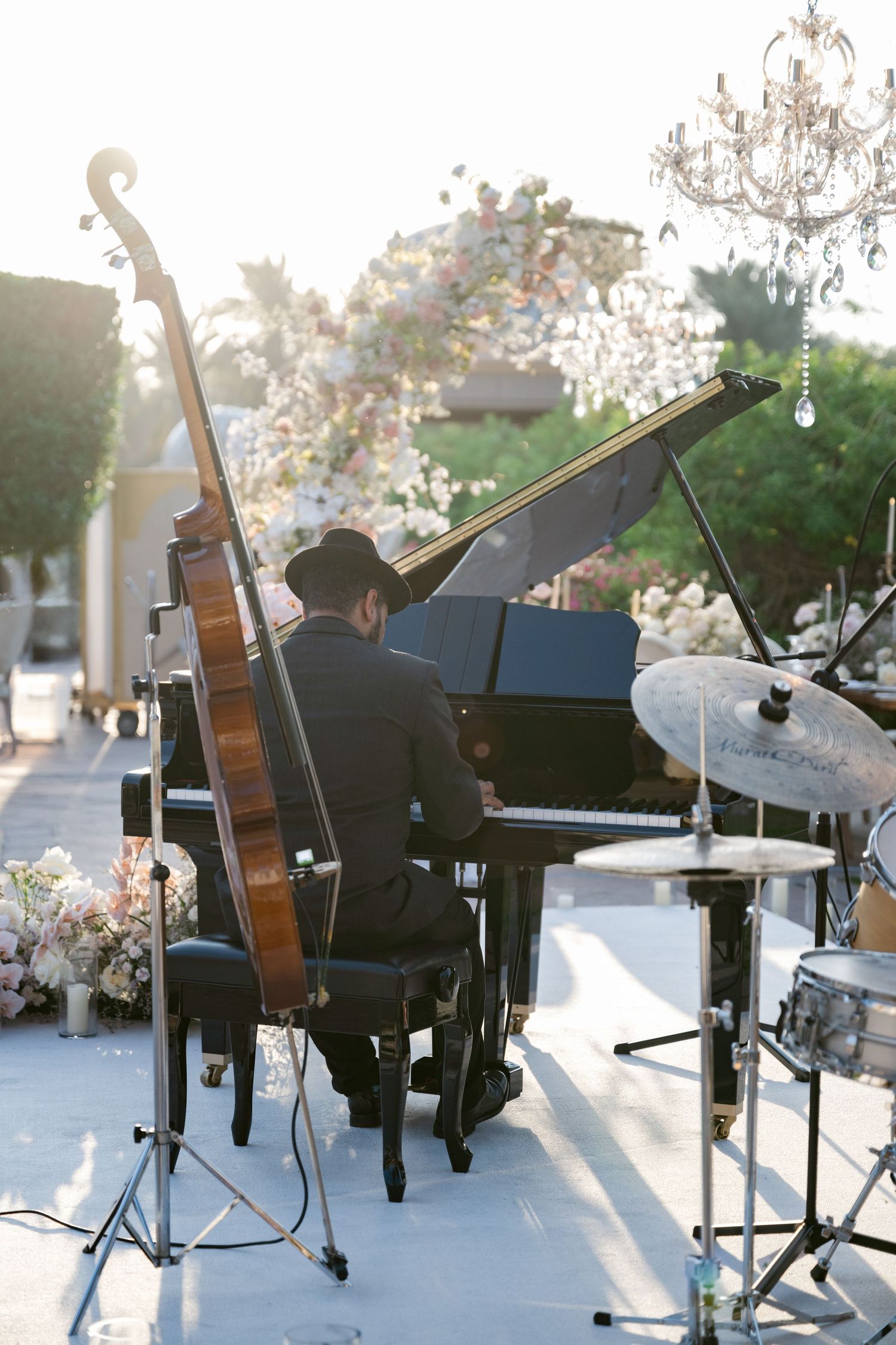 Musician performing on grand piano outdoors at elegant event with floral decorations.