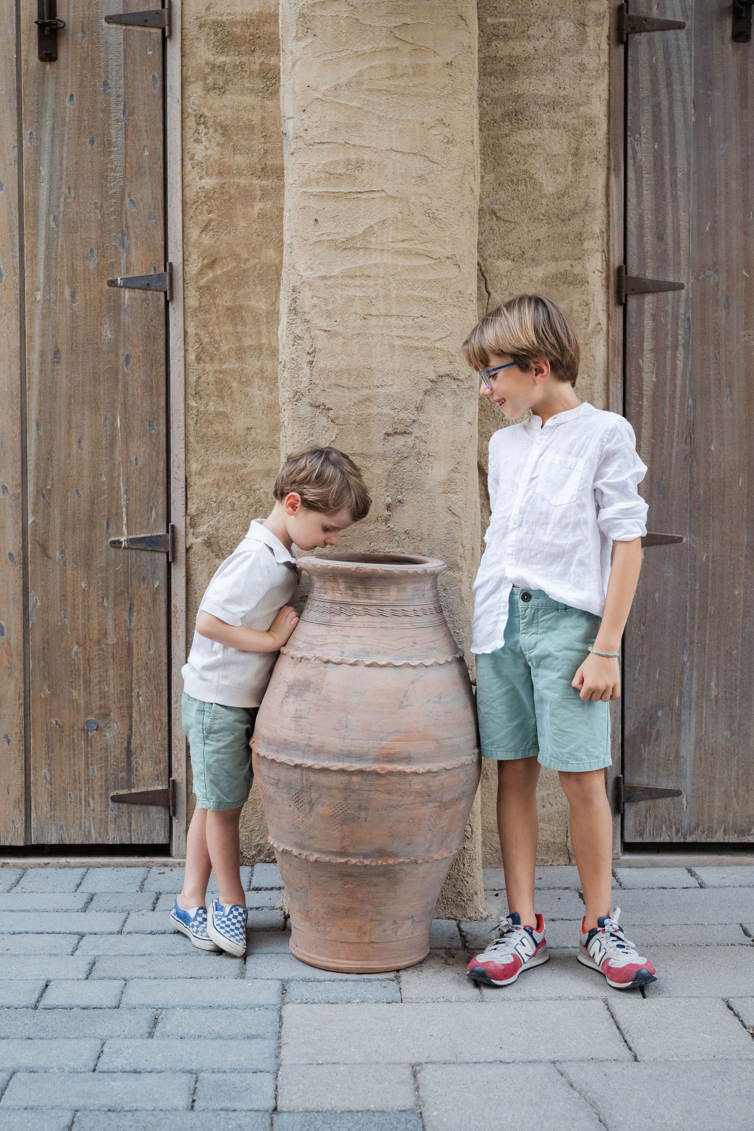 Children examine a large terracotta pot in a historic stone hallway.