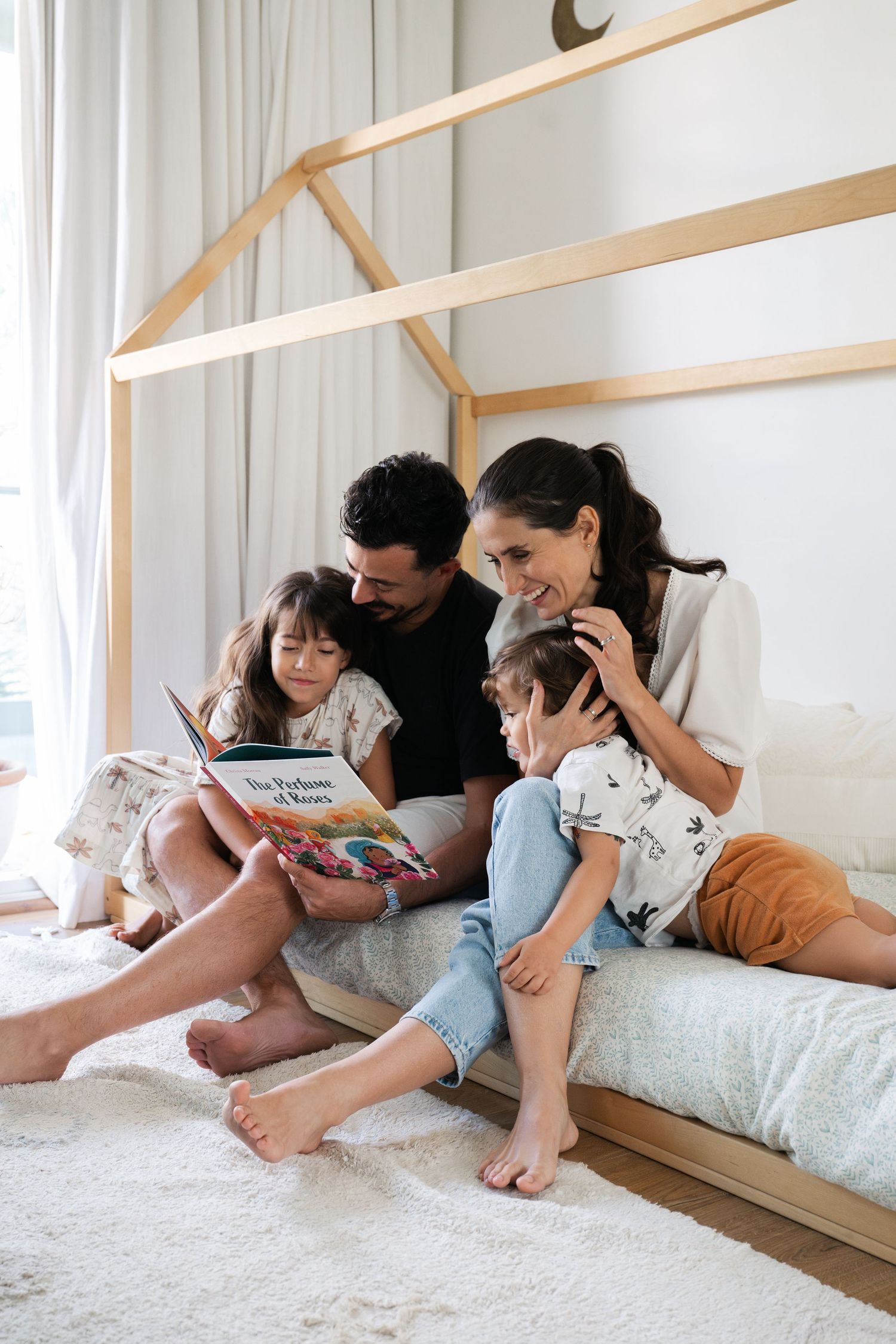 Family reading books together while relaxing on floor mattress in bright room.