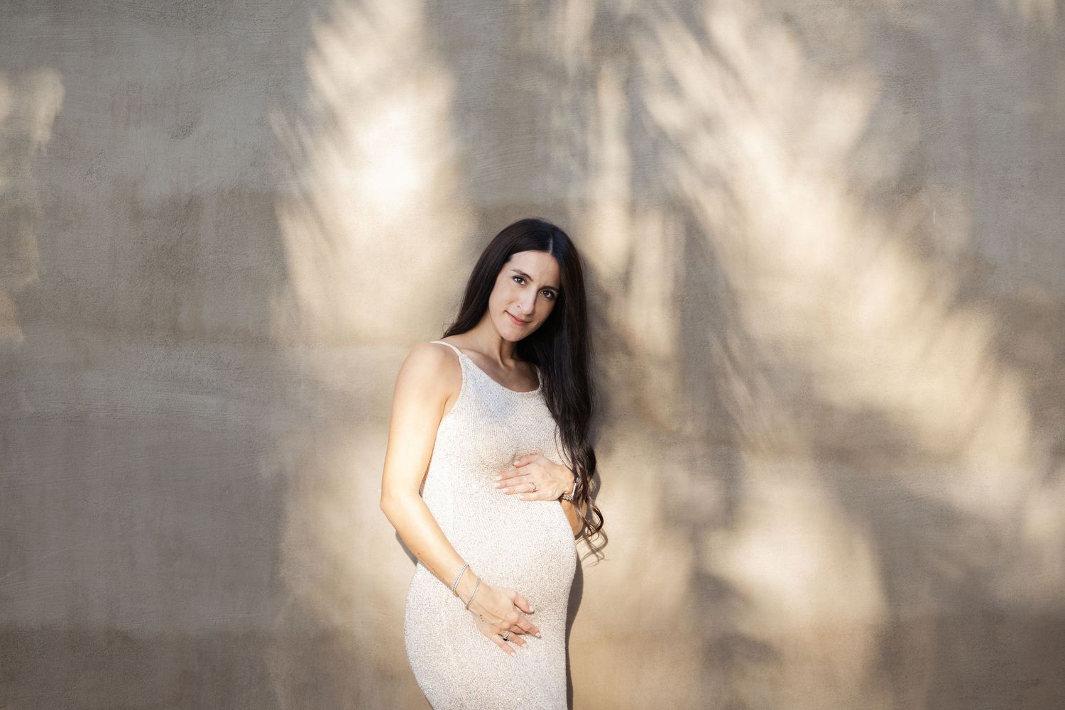 Elegant maternity portrait with dramatic shadow play on white wall.