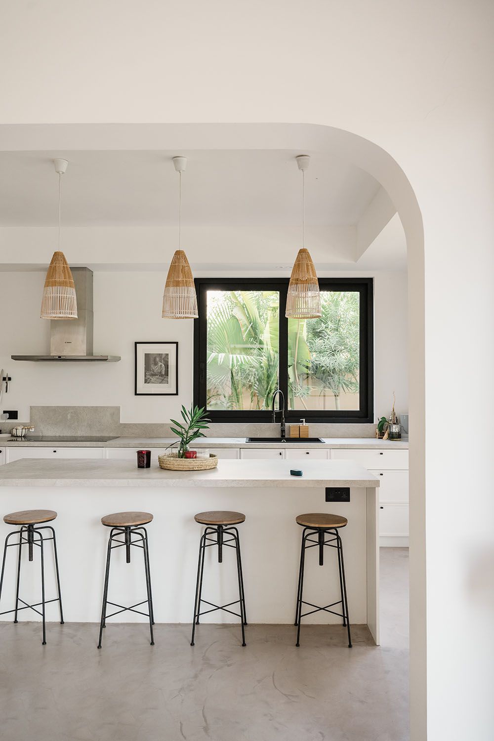 Minimalist white kitchen with four wooden bar stools and pendant lighting along a sleek countertop.
