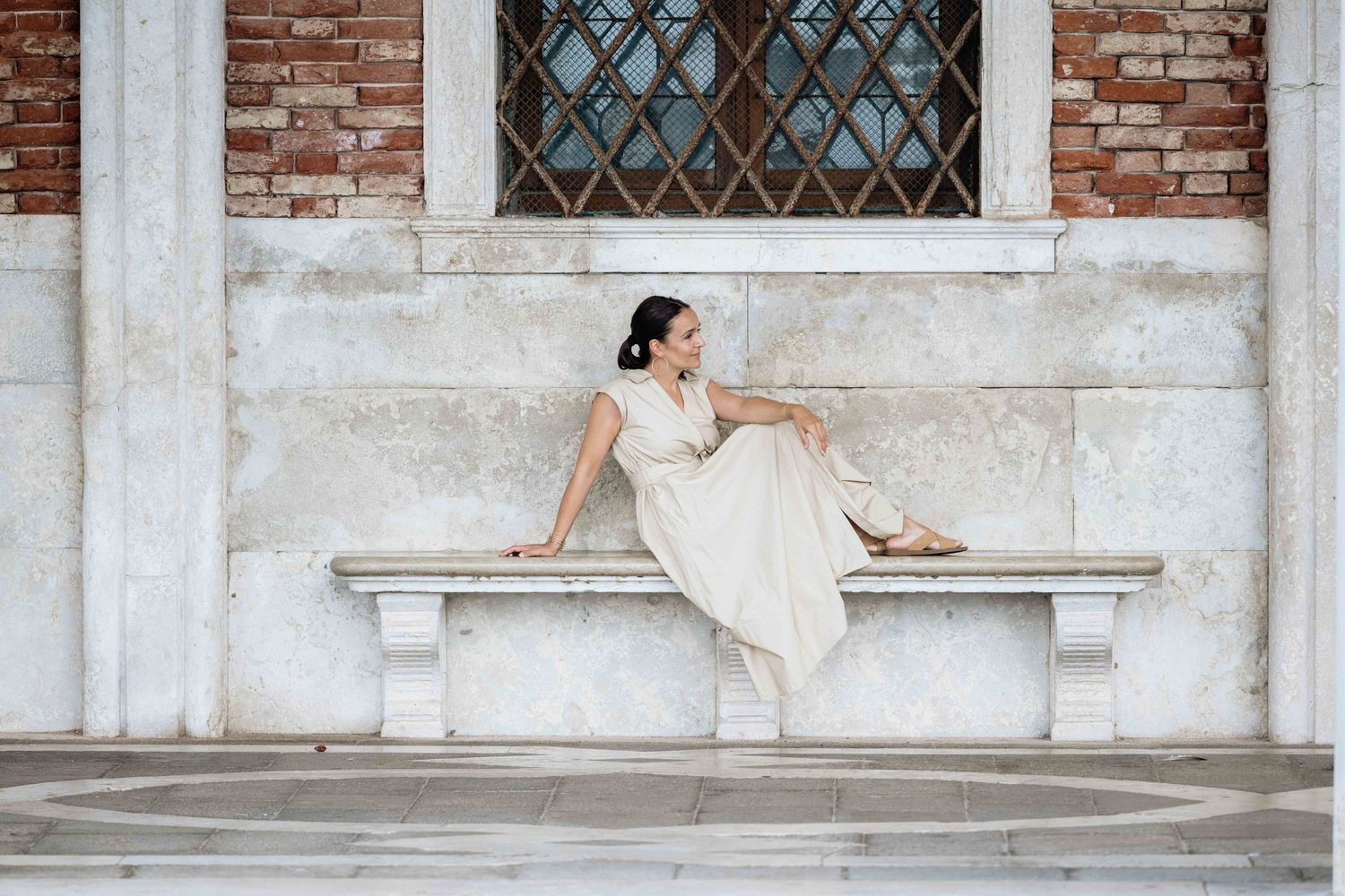 Elegant pose against traditional Venetian architecture with exposed brick and ornate window details.