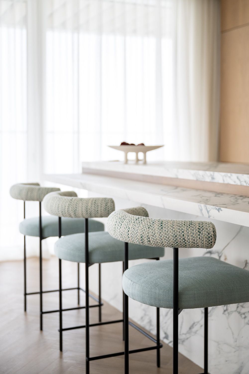 Modern white marble table with sleek gray upholstered bar stools featuring black metal frames in a bright interior.