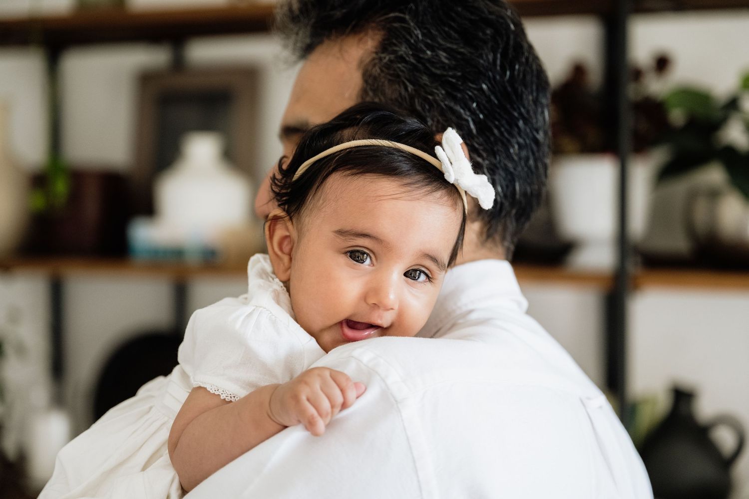 Sweet interaction between parent and baby in white against neutral background.