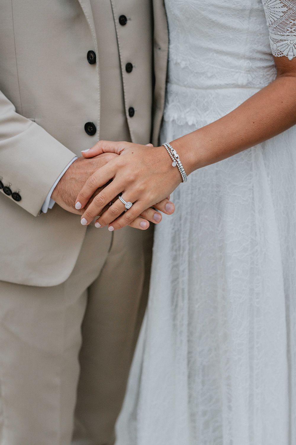 Close-up details of wedding attire showing hands, rings, and formal wear in light colors.