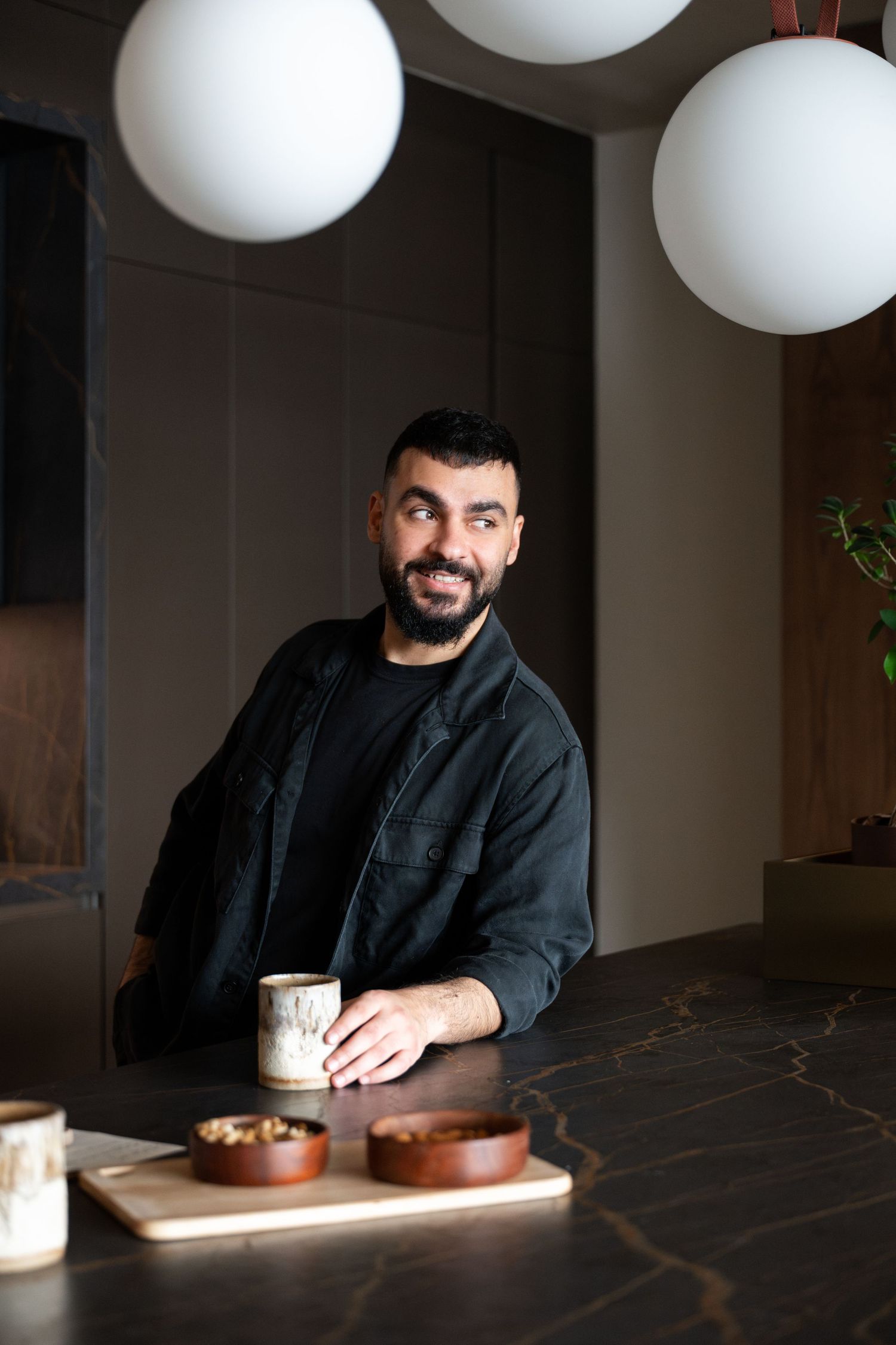 Person enjoying coffee and snacks at a dark marble table with modern white pendant lighting.