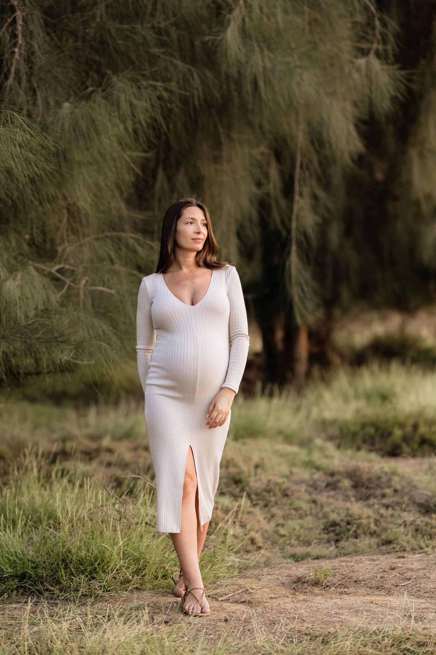 Maternity photography session in a white dress against natural outdoor backdrop.