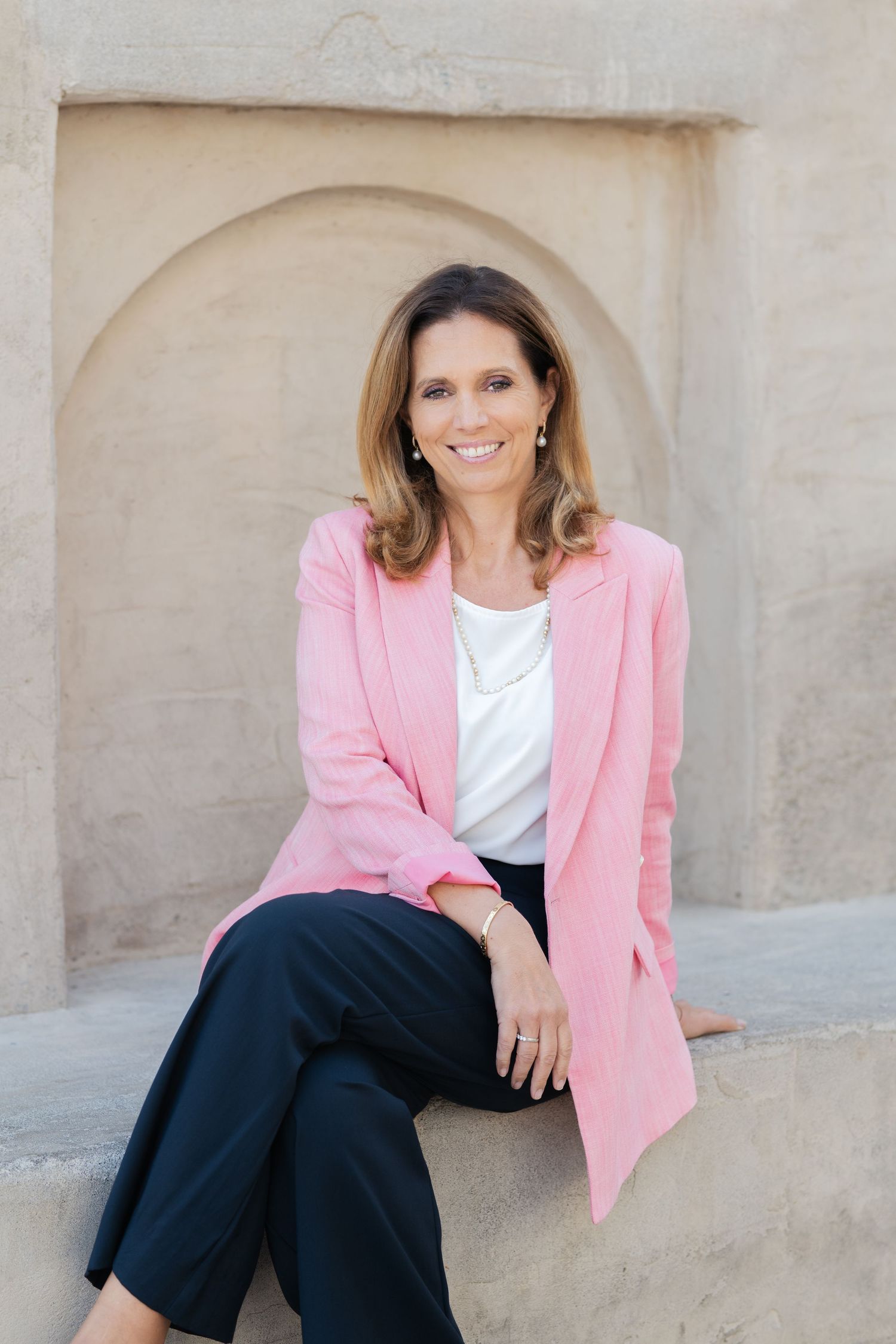 Business casual portraits with pink blazer against neutral wall.