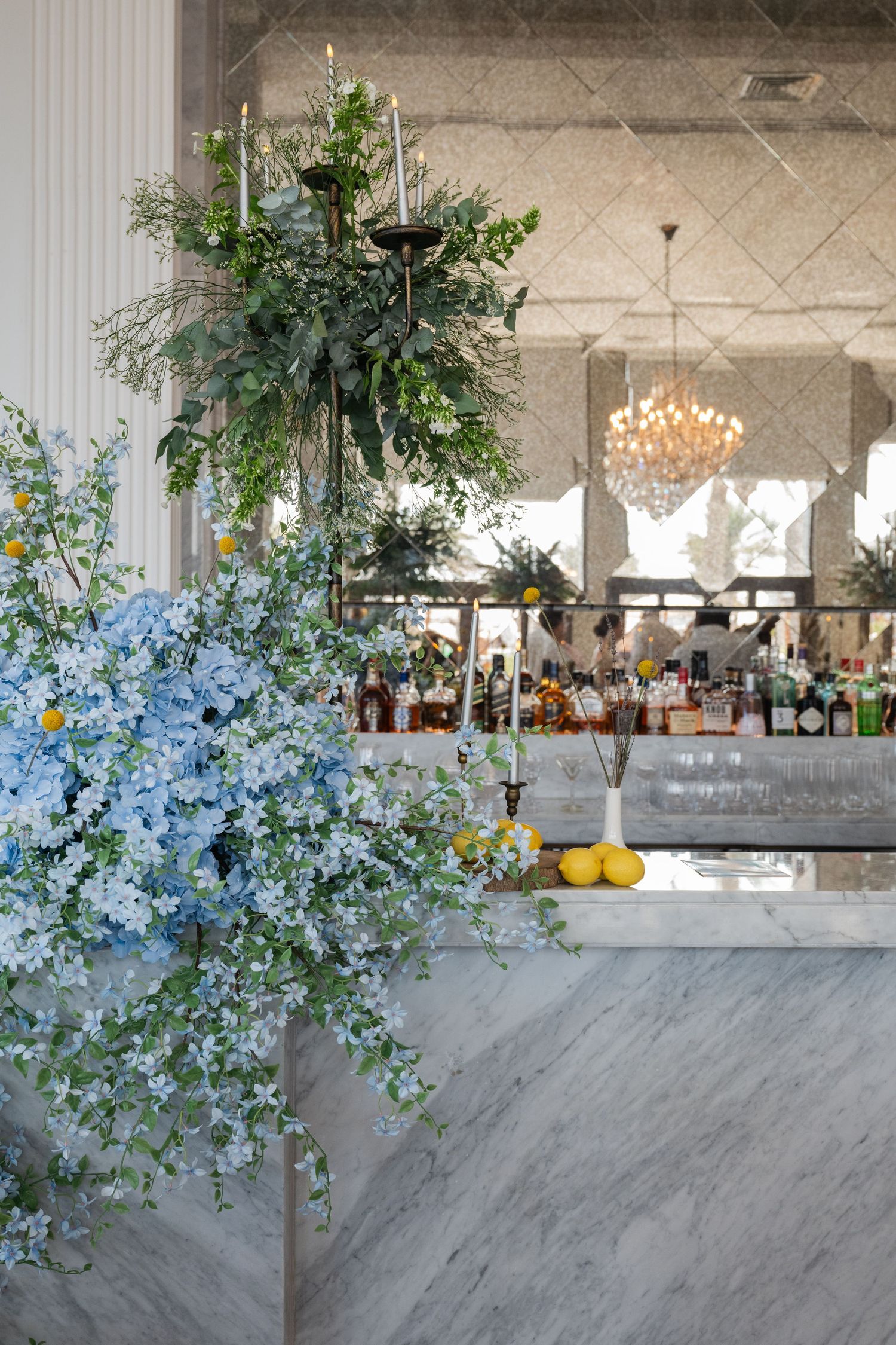 Luxurious event space with blue florals, hanging greenery, and crystal chandelier.