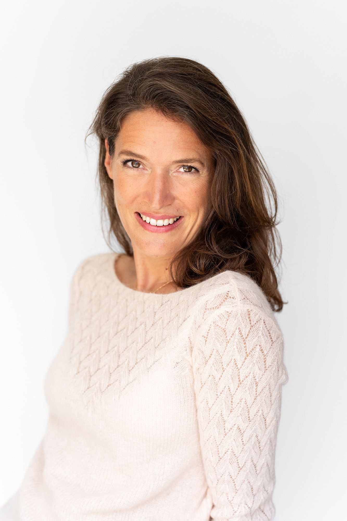 Person wearing a white knit sweater smiles warmly against a light background in a studio portrait series.