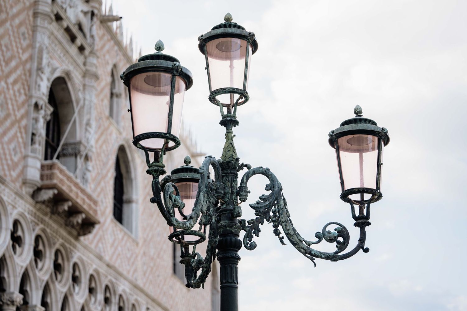 Ornate vintage street lamps with decorative metalwork line a historic building facade in Venice.