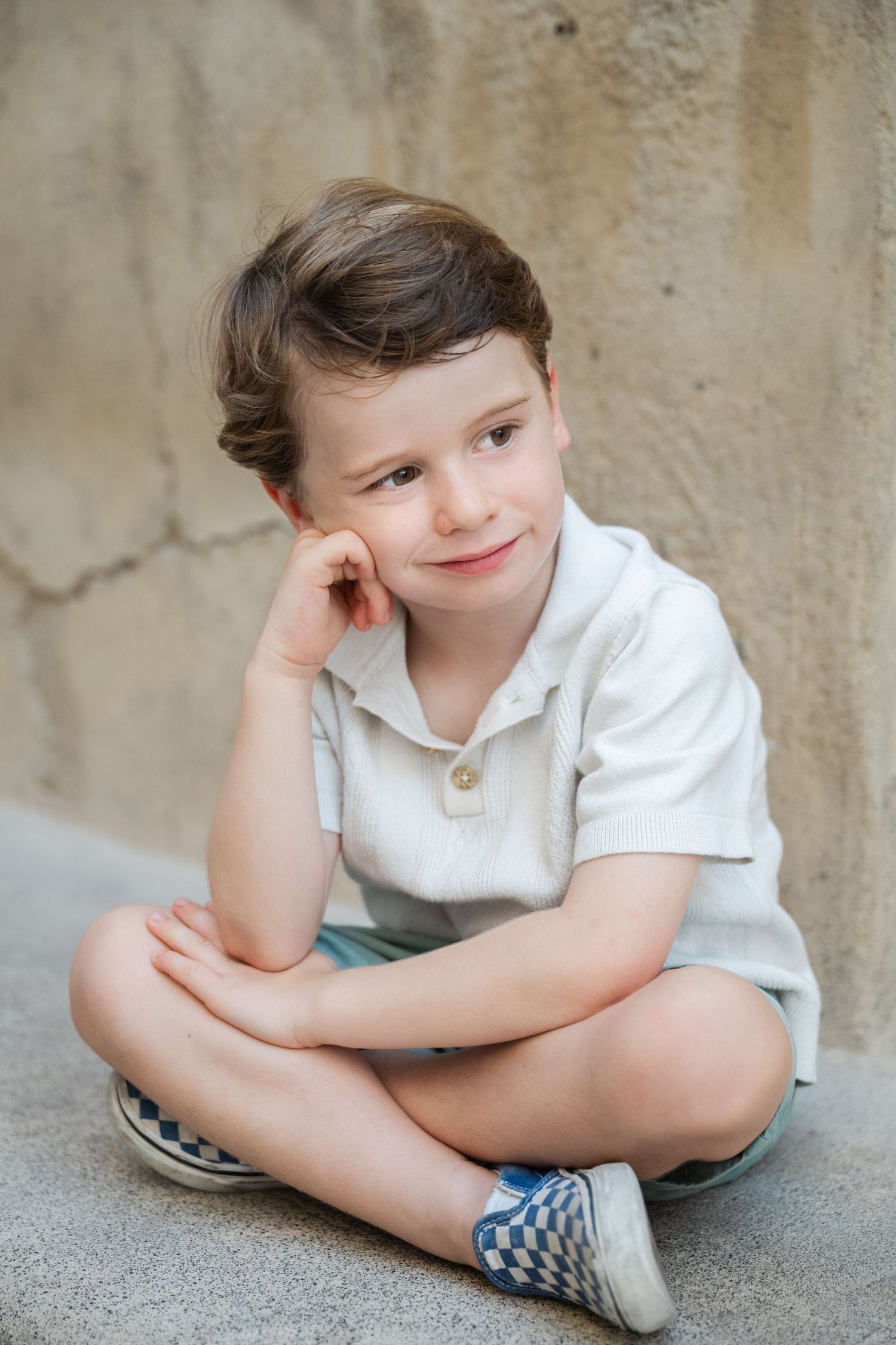 Child in white shirt sitting casually against stone wall.