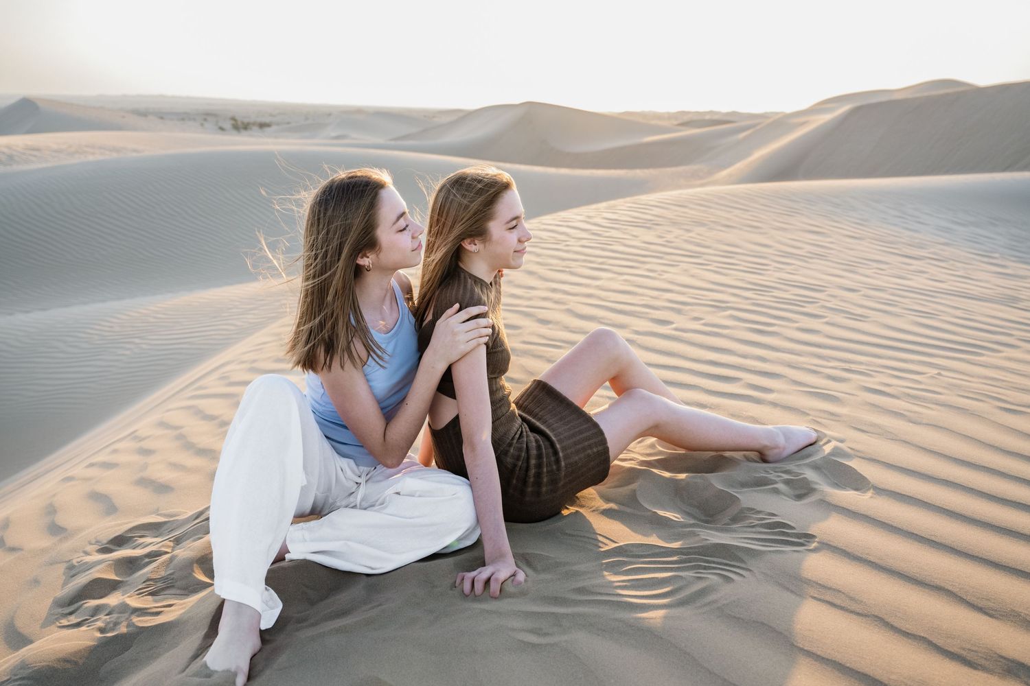 Two people relaxing together on sandy desert dunes during golden hour.