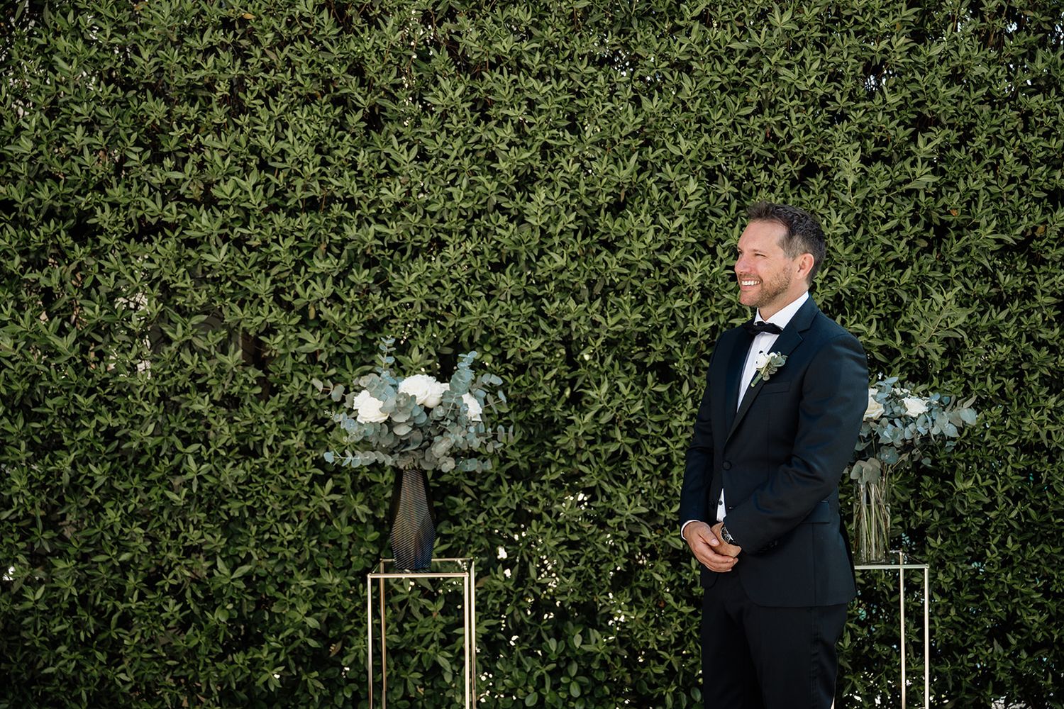 Wedding ceremony setup with greenery backdrop and white floral arrangements.