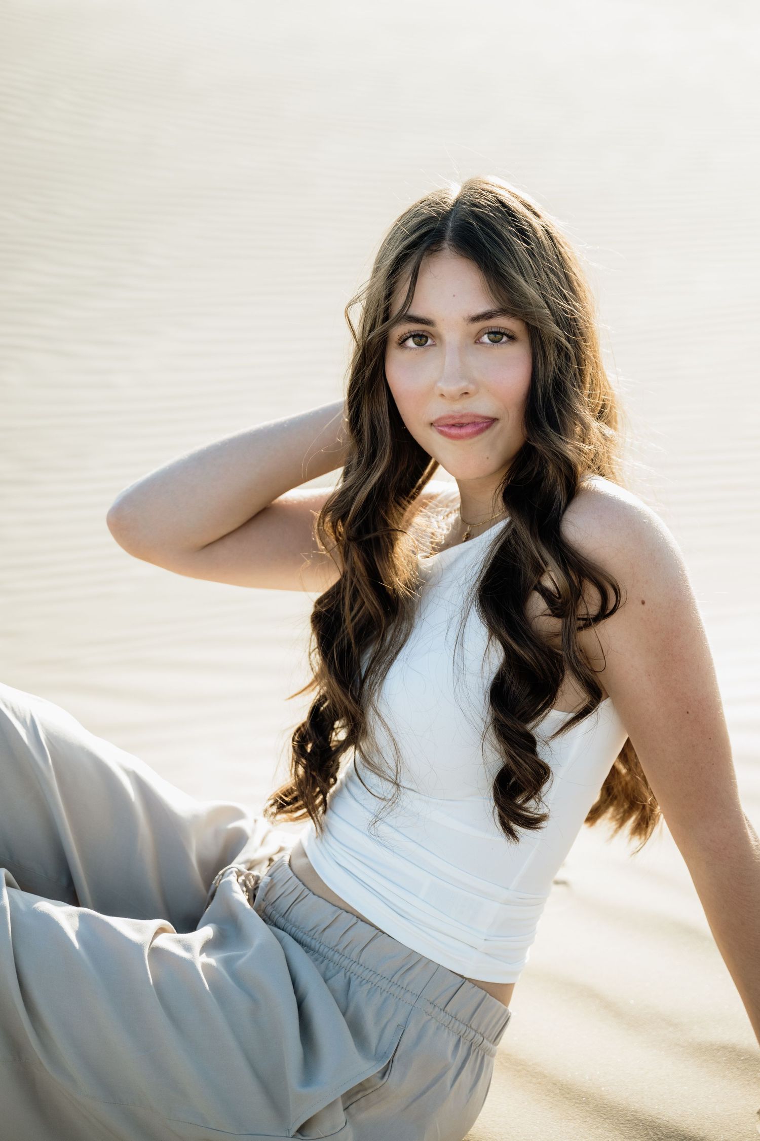 Person in white top poses elegantly on sand dunes during golden hour.