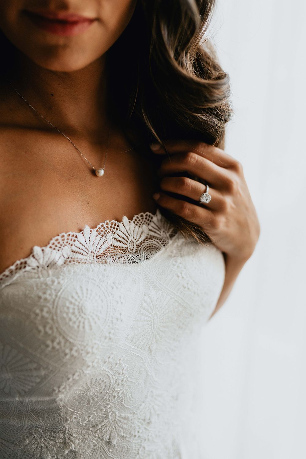 Detail shot of delicate lace bodice with heart necklace and engagement ring.