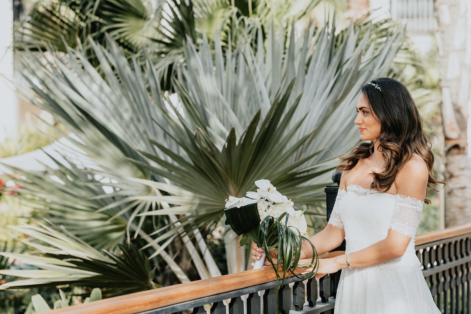 Romantic bridal portrait against tropical palm leaves with white orchid bouquet.