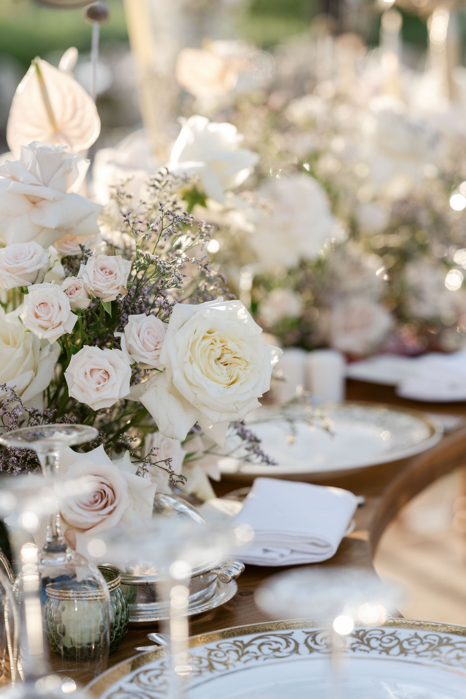 Luxurious table setting with white roses and delicate place settings on ornate plates.