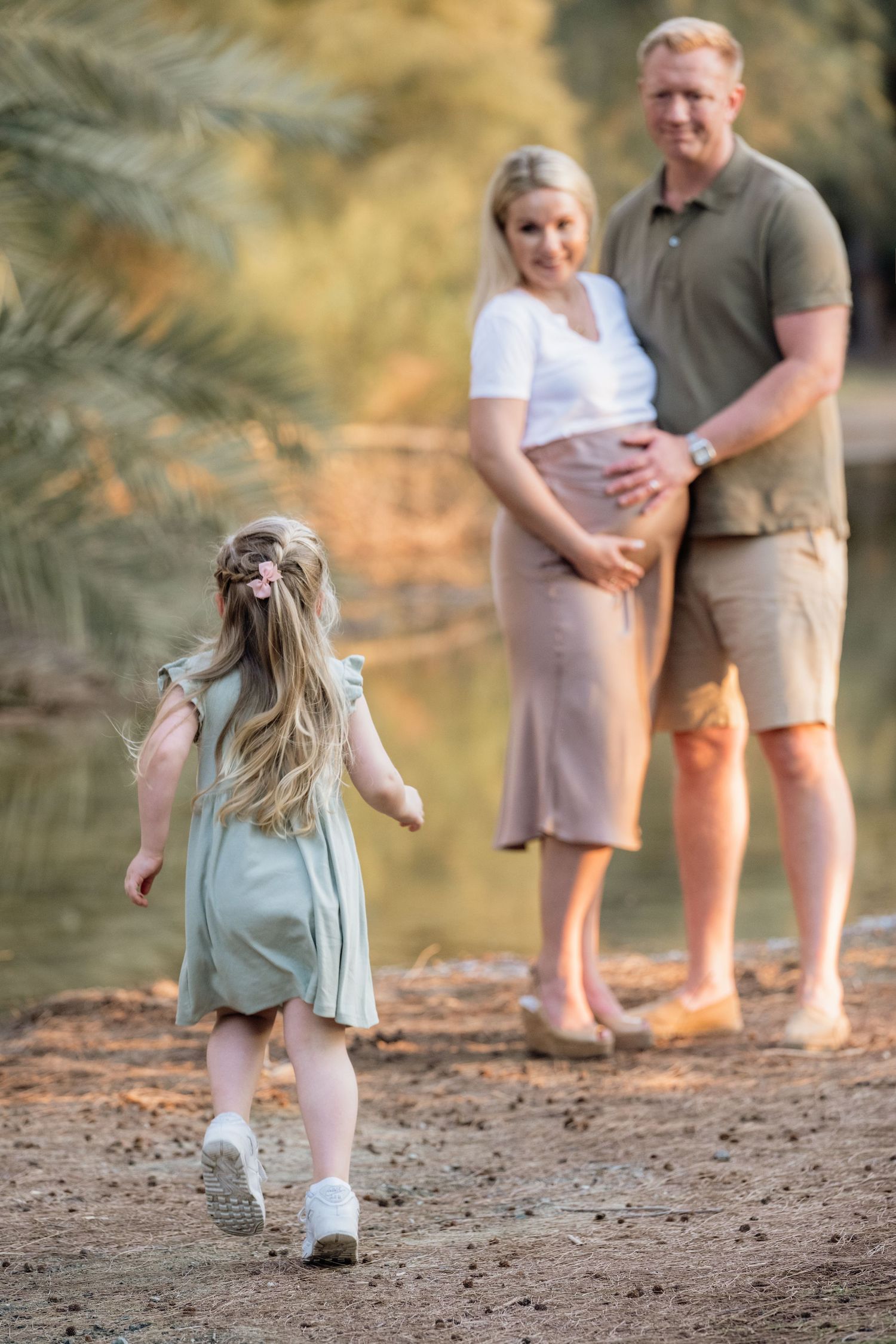 Child runs playfully on beach while parents watch in background during golden hour.
