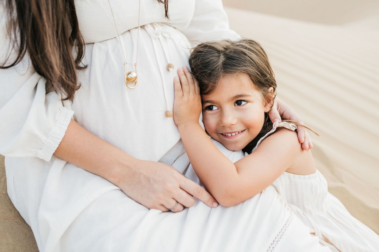 Intimate maternity photoshoot with soft lighting and white clothing on beige background.