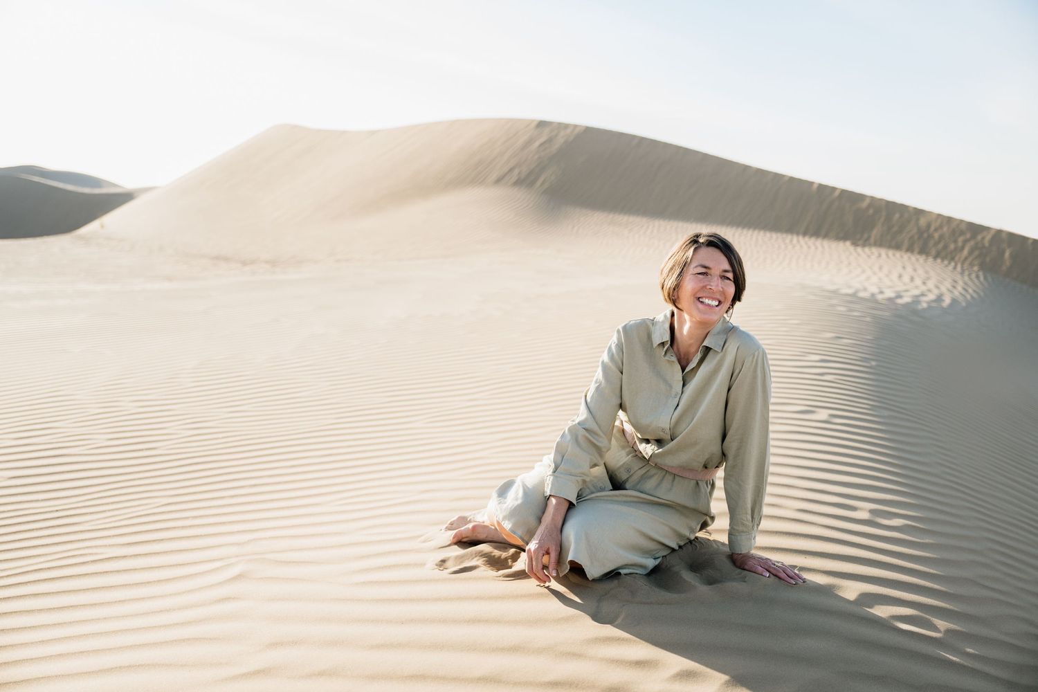 Person in light colored clothing reclining on textured sand dunes.