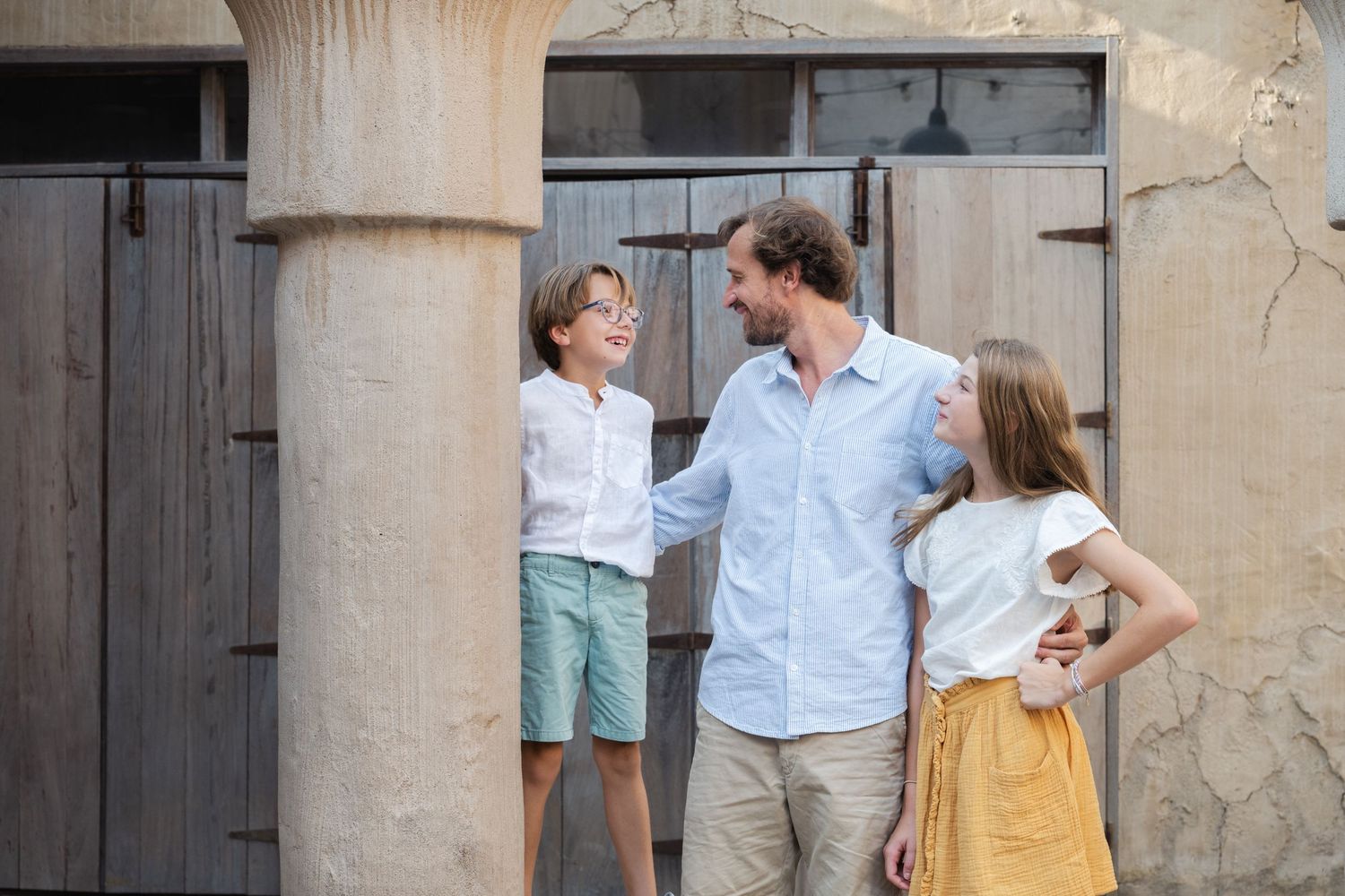 People interacting casually in front of a rustic stone wall with columns.
