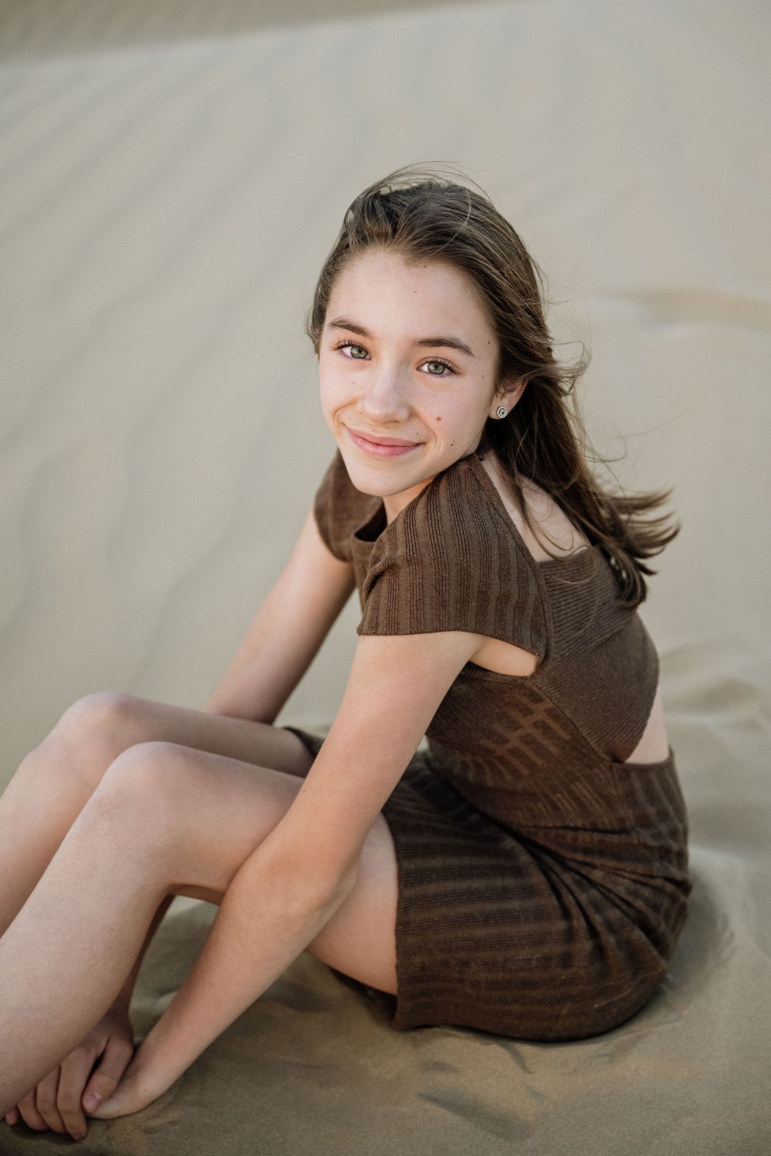 Person in brown dress reclining on textured sand dunes during photo session.