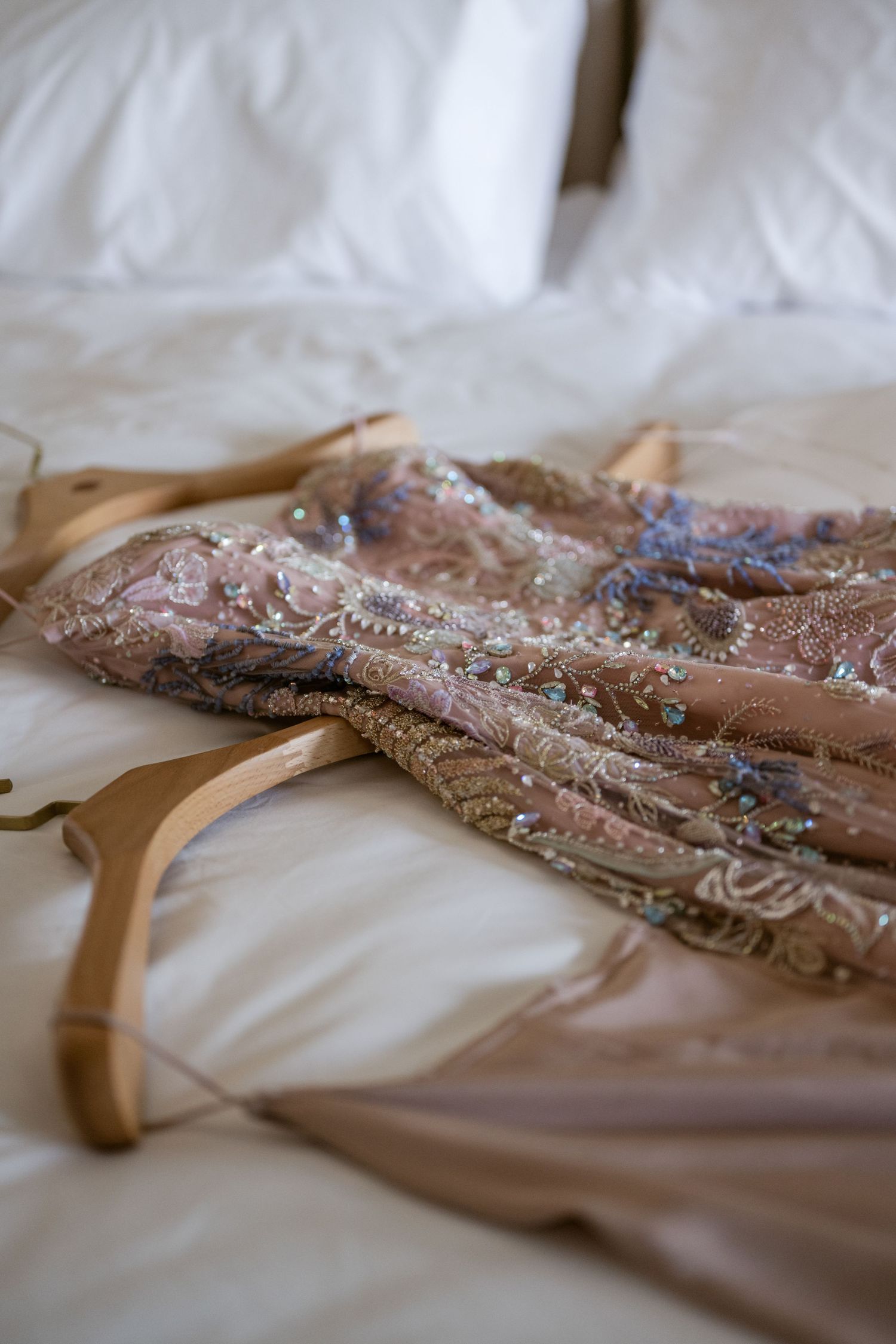Beaded champagne-colored formal dress with intricate embellishments laid flat on white bedding.