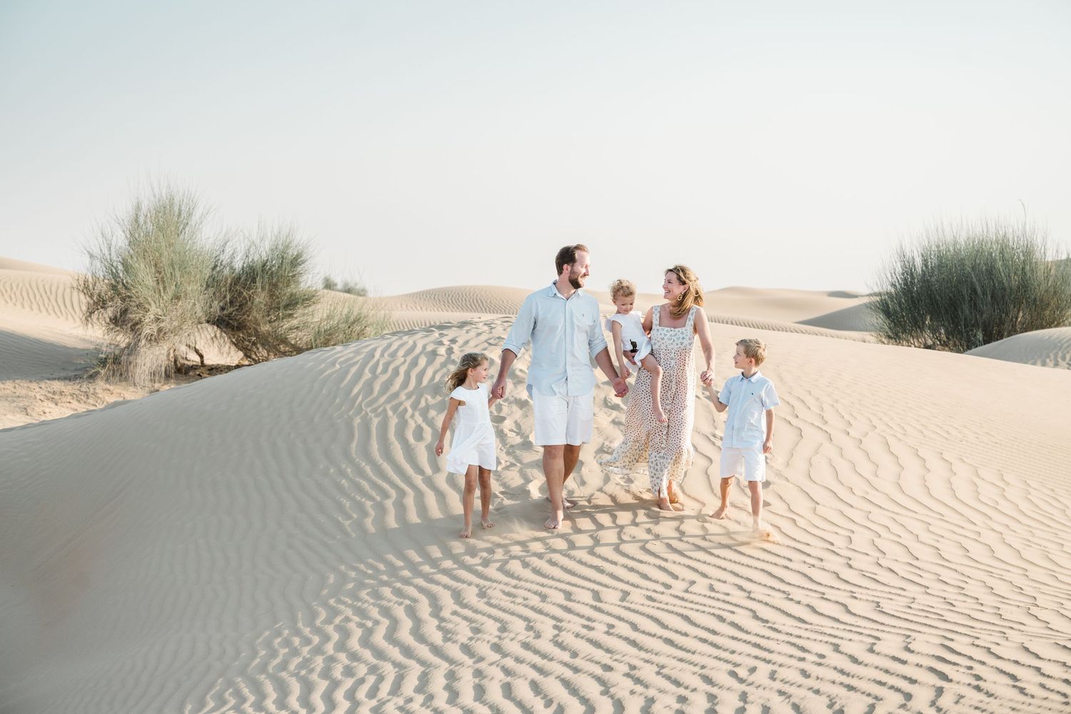Family walking together on rippled desert sand dunes in coordinated white and blue outfits.