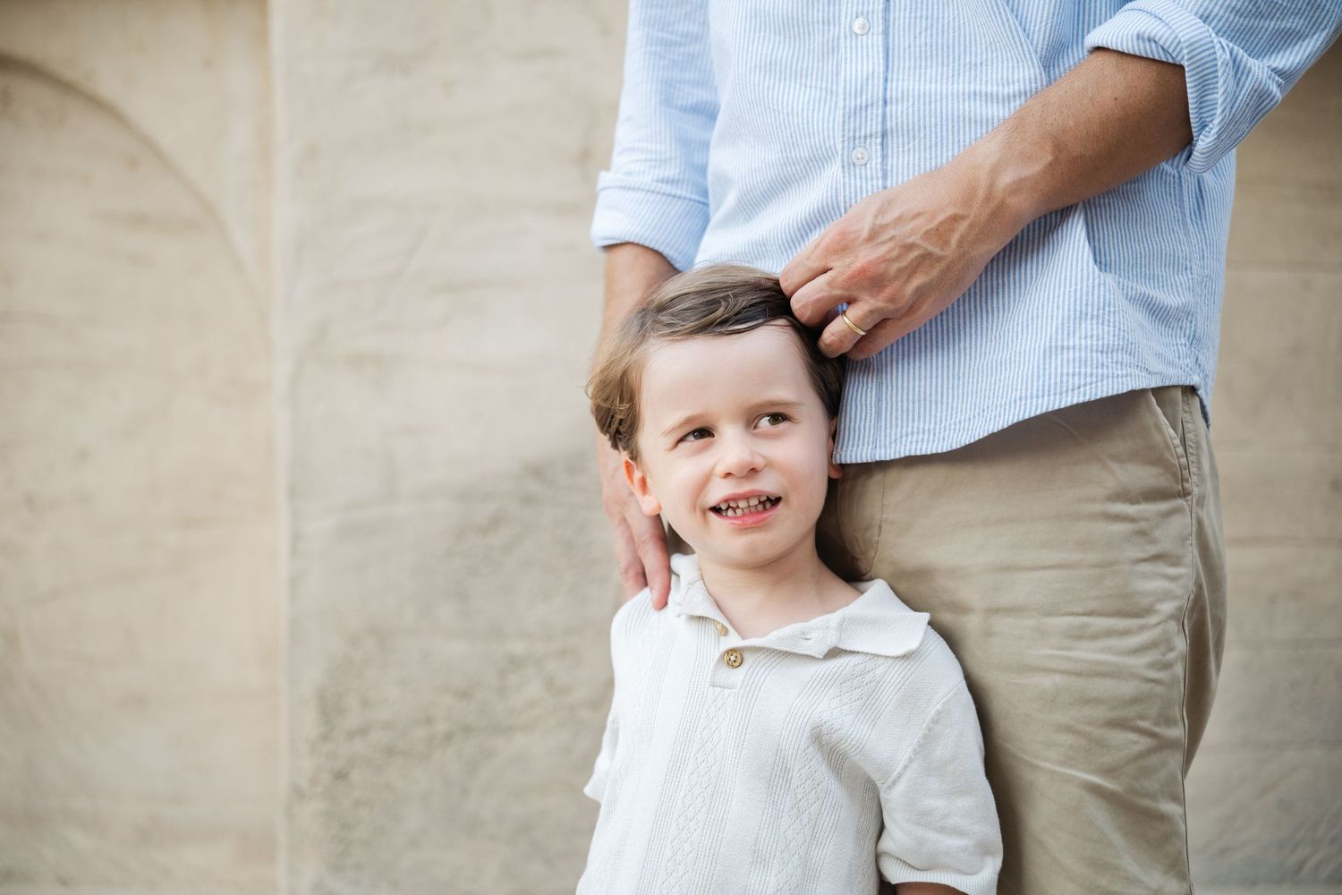 Tender interaction between adult and child against neutral wall backdrop.