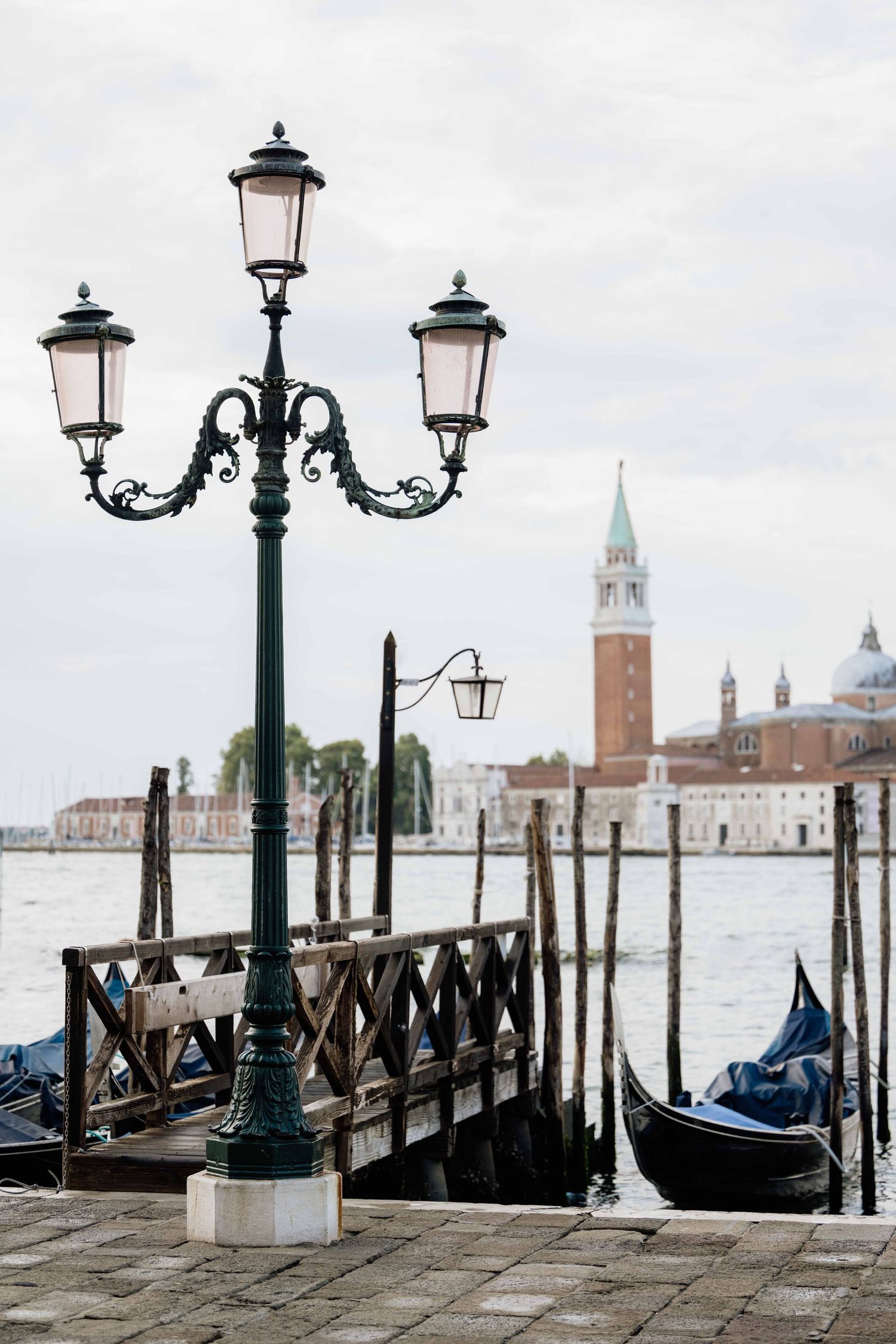 Vintage-style lampposts and gondolas line Venice's waterfront with San Giorgio Maggiore in the distance.