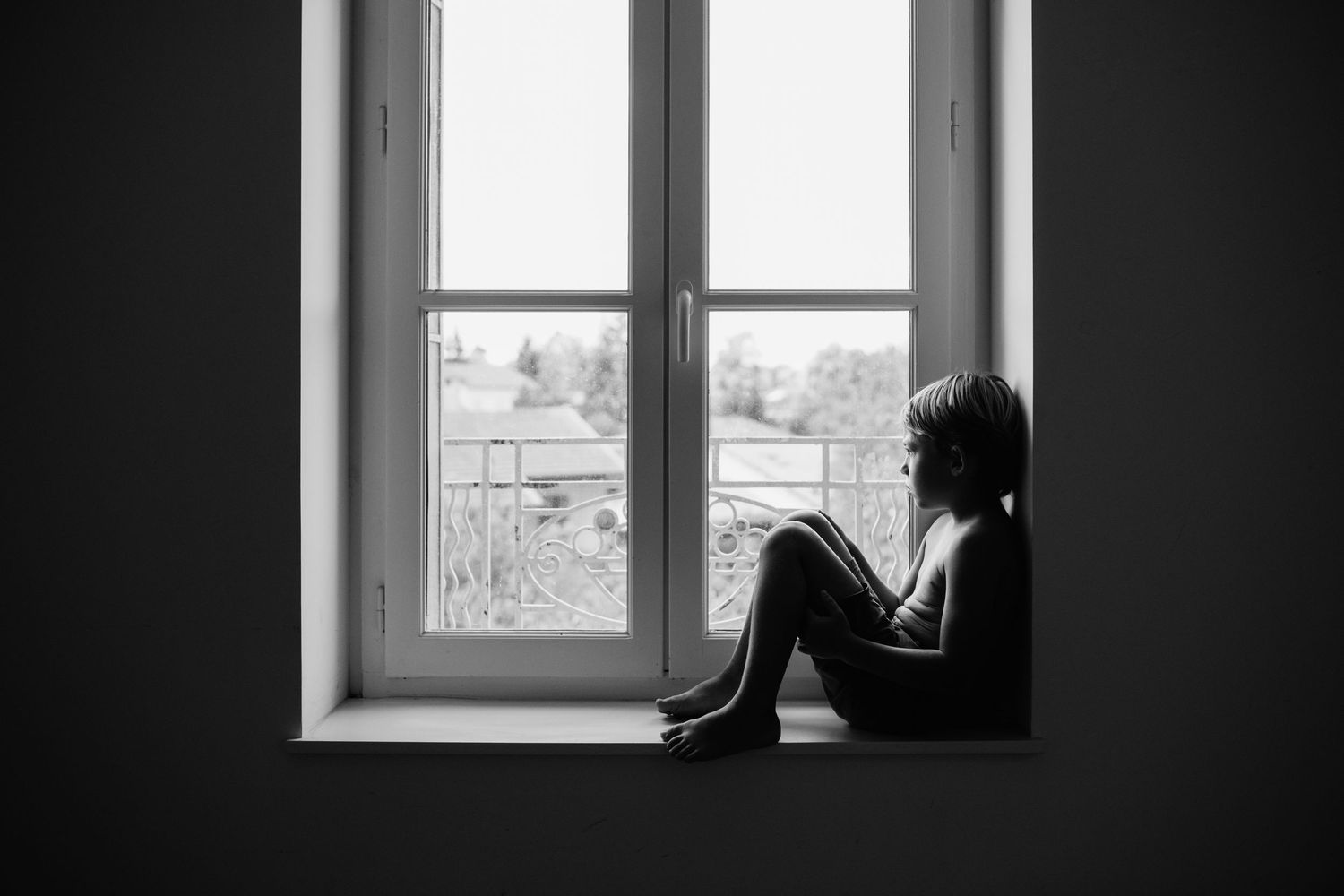 A dramatic black and white composition of a boy's portrait sitting beside a window