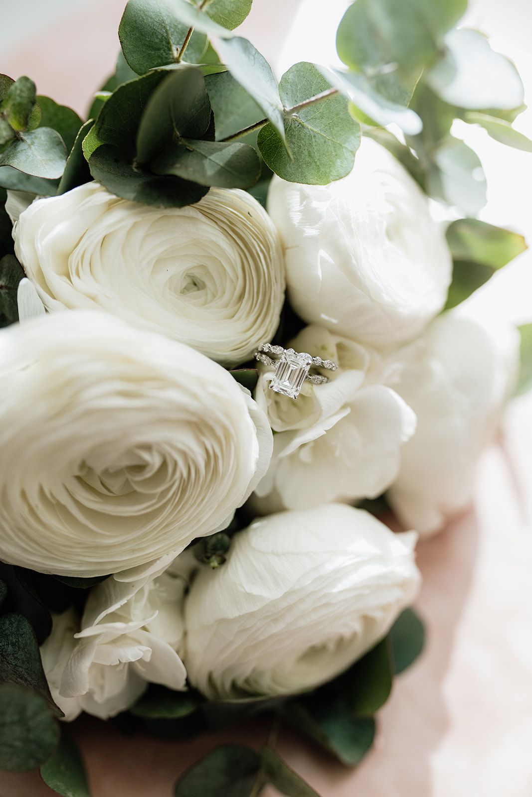 Close-up of white ranunculus bouquet with eucalyptus leaves and diamond ring.