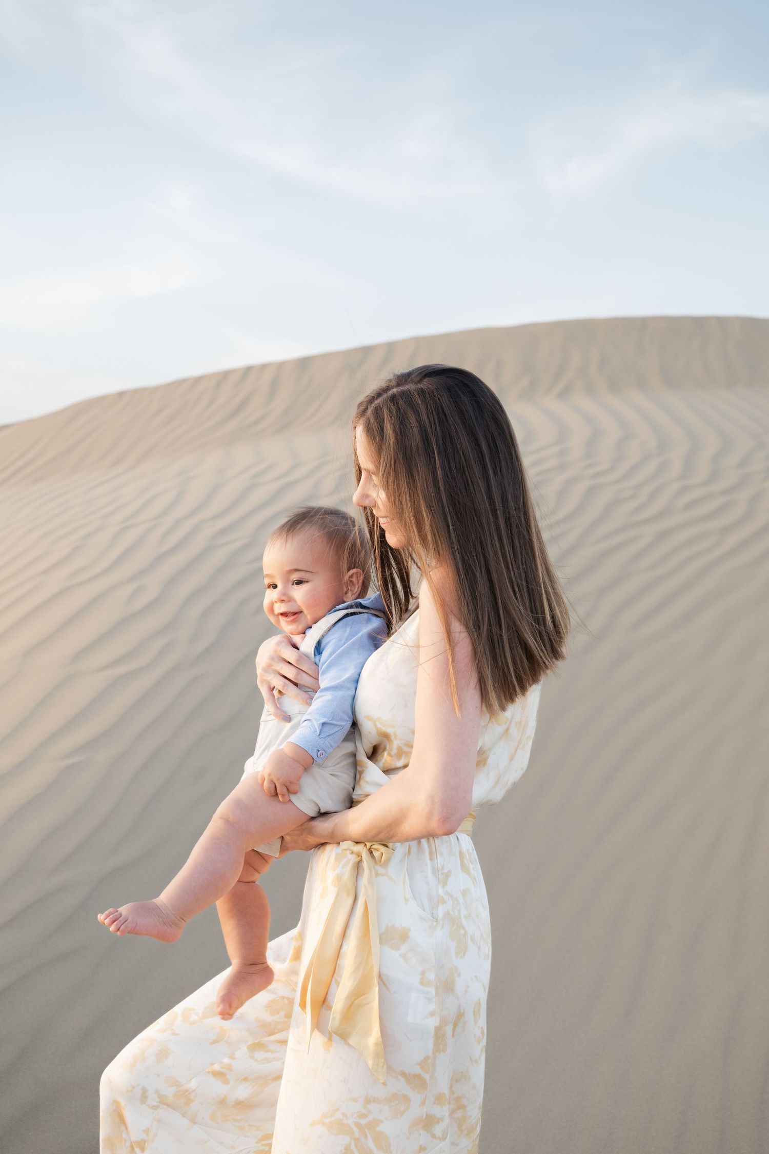 Mother and child sharing joyful moments against rippled sand dunes at sunset.