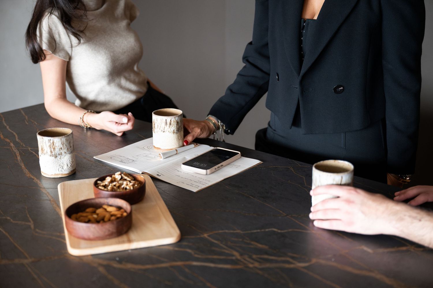 Hands arranging items on a dark marble surface with dramatic lighting and white decor.