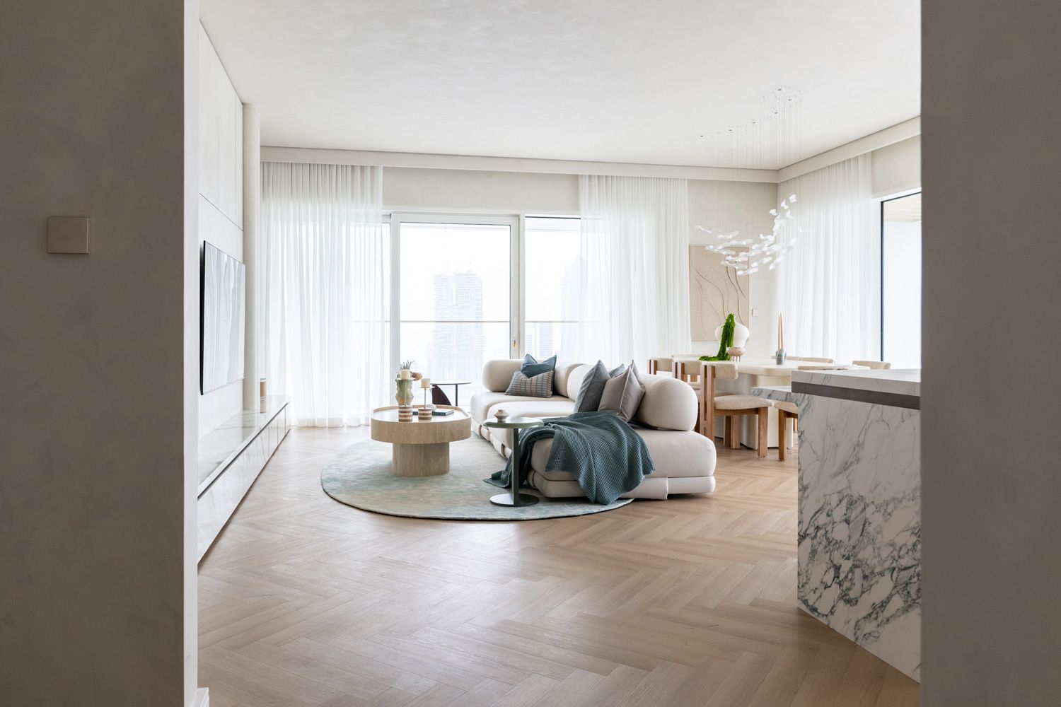 Modern empty apartment interior with white walls, light wood flooring, and large windows offering natural light.