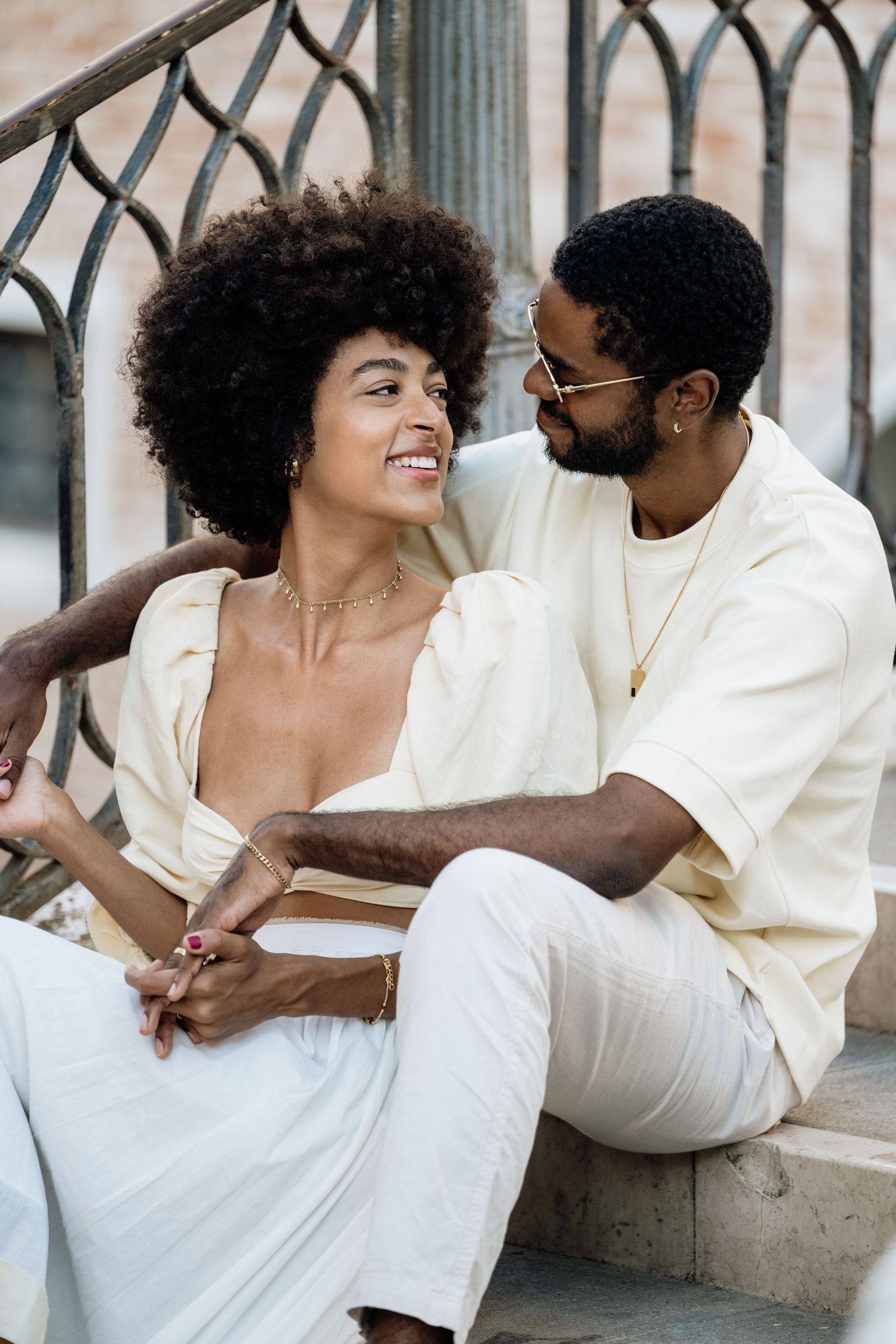 Couple in white clothing sharing intimate moments while sitting together against a wall.