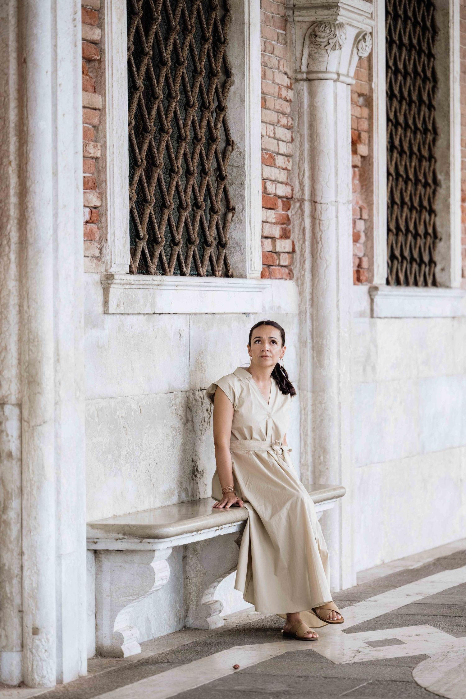 Light-colored dress creates striking contrast against the historic Venetian colonnade and brick walls.
