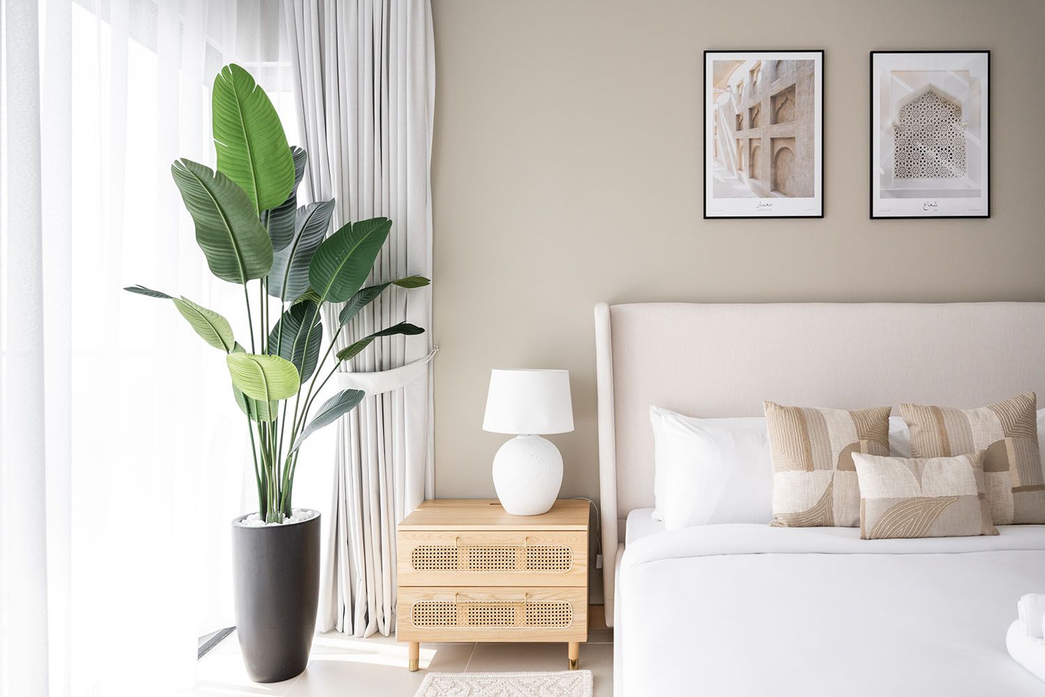 Contemporary bedroom with beige walls, white bedding, and potted palm plant near window.