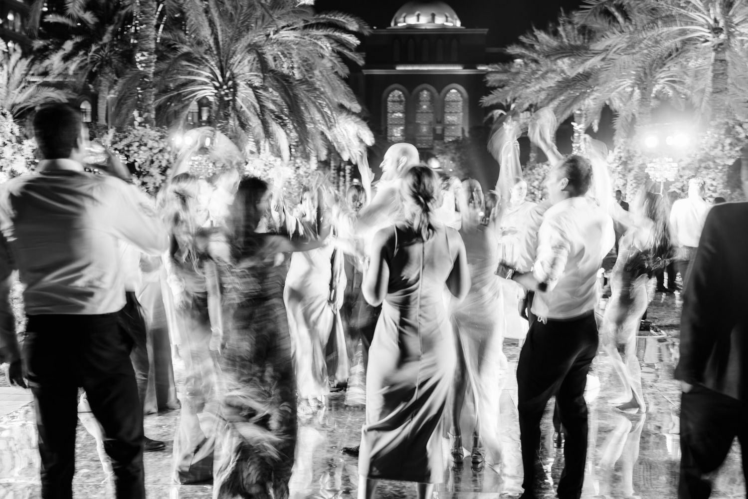 Lively wedding reception dance floor filled with guests celebrating under palm trees.