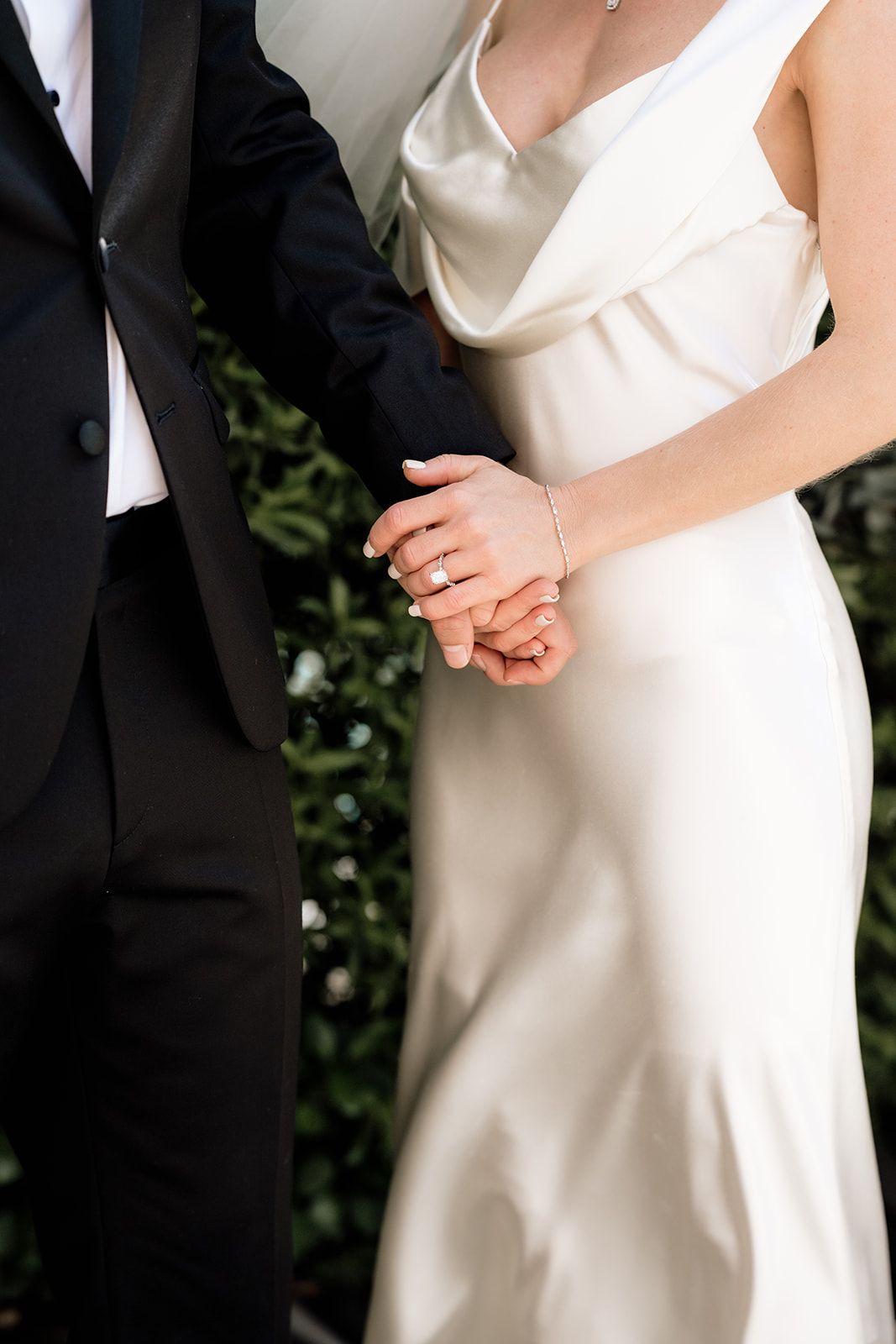 Details of elegant white wedding dress and formal attire against greenery backdrop.