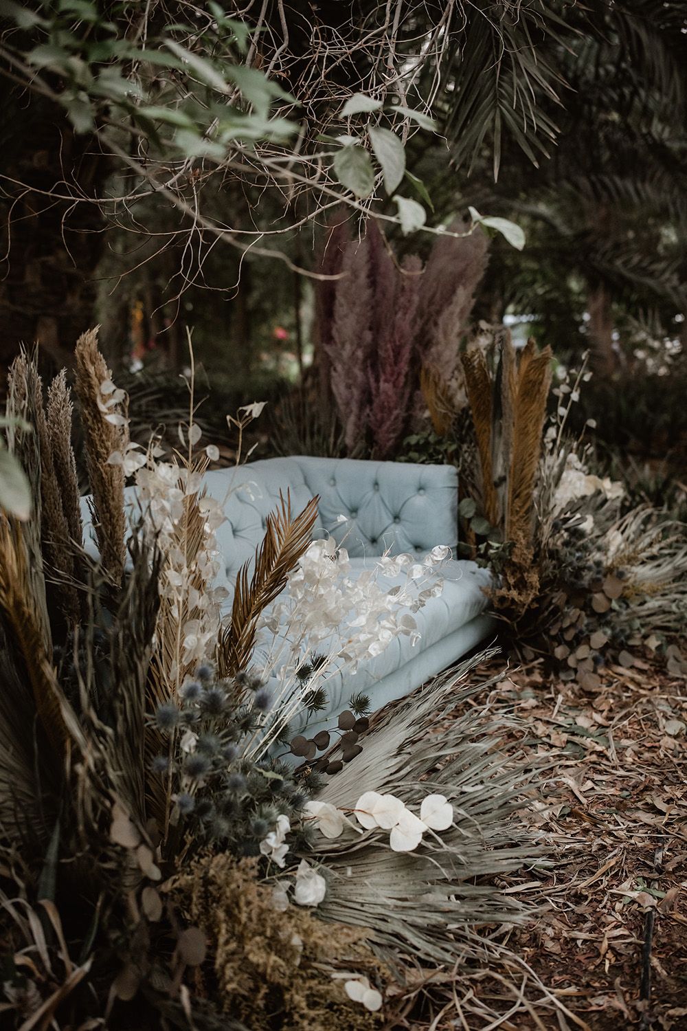 Light blue tufted vintage sofa nestled among trees and fallen leaves.